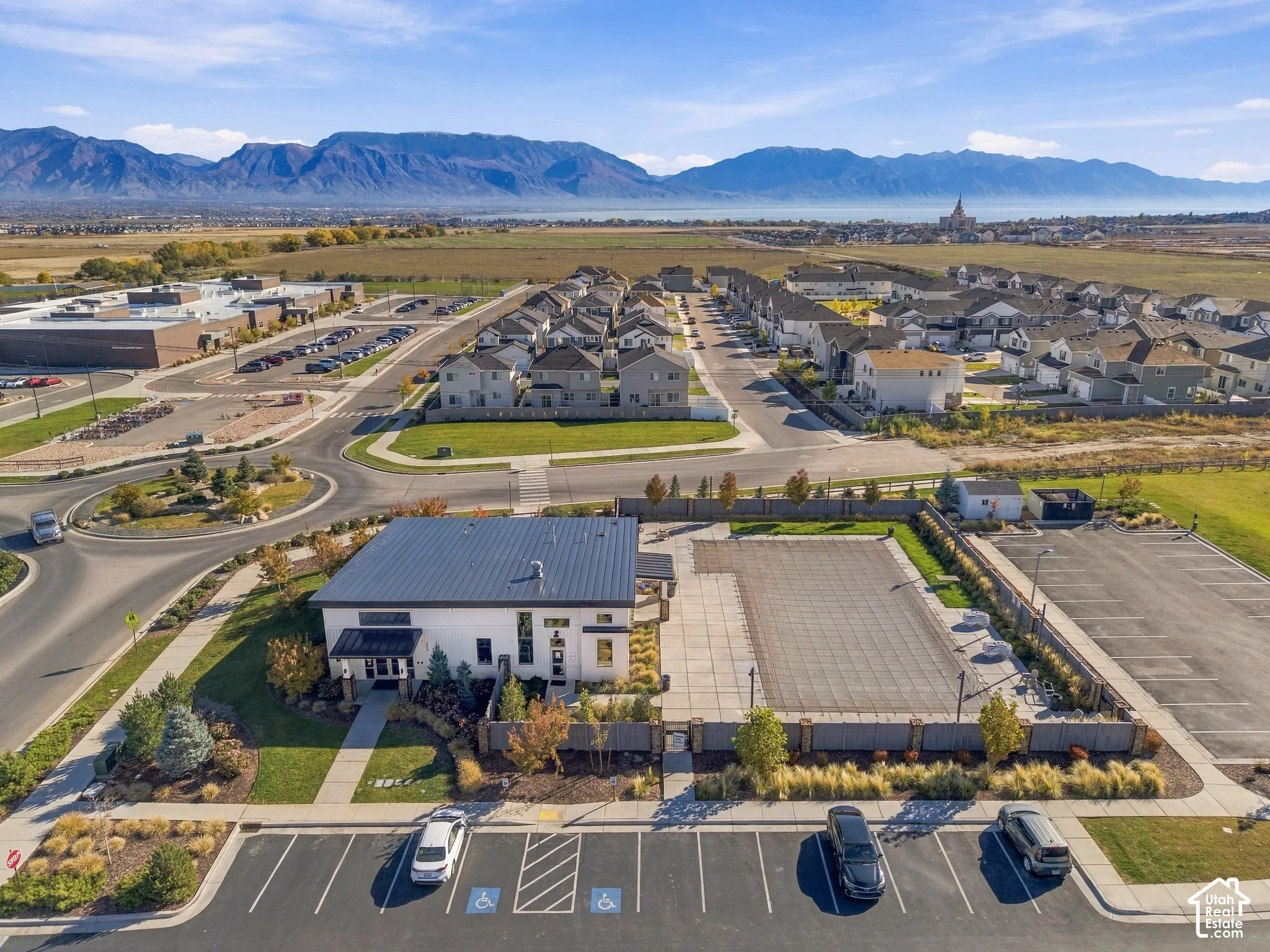 Aerial perspective featuring a clubhouse with a metal roof, an expansive hardscaped courtyard, stone pillar fencing, designated parking facilities, and mountain range scenery