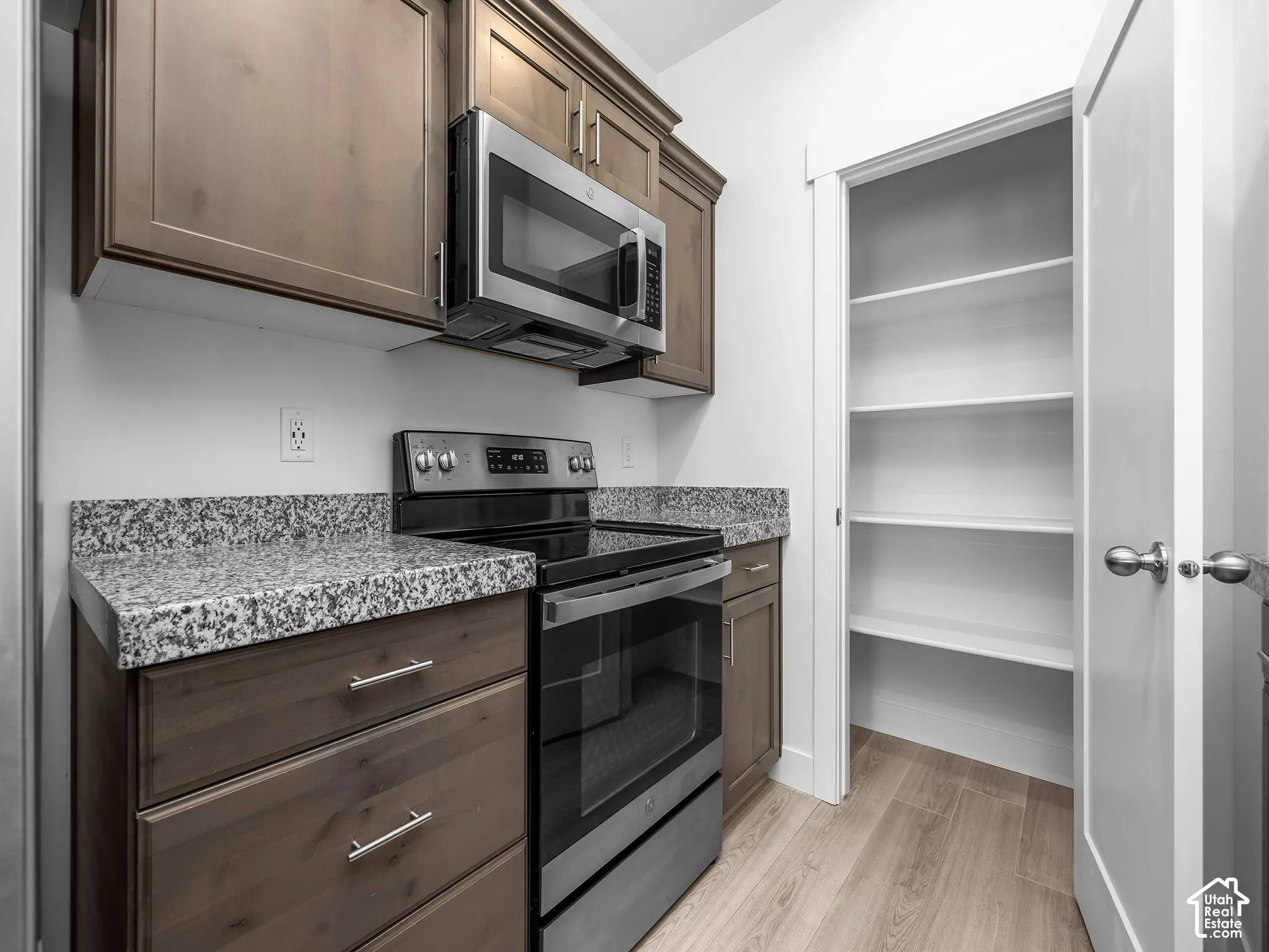 Kitchen featuring stained wood cabinetry, stone-finish countertops, stainless steel appliances, and a dedicated pantry with built-in shelving