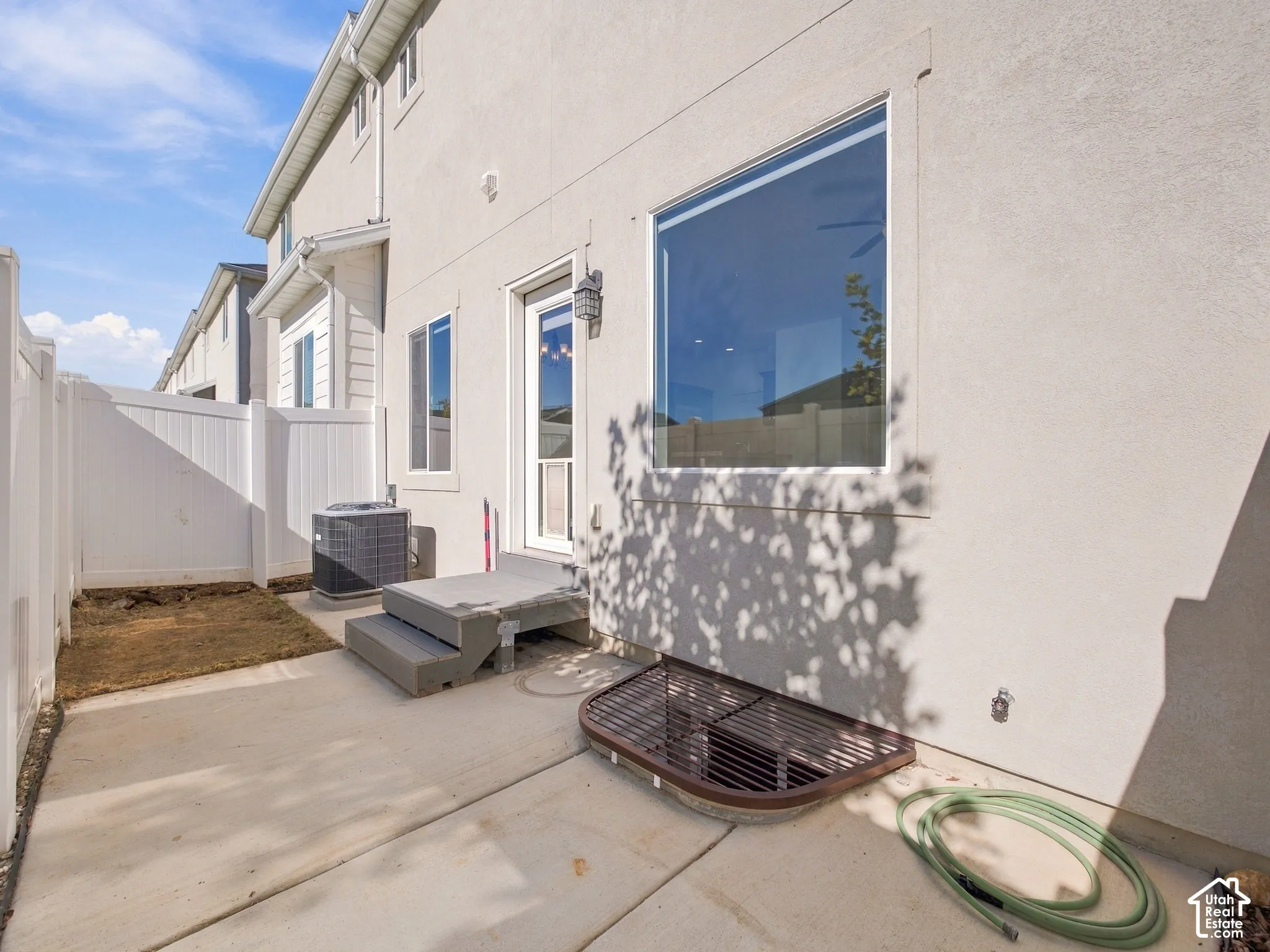 Stucco exterior finish with concrete patio, enclosed white vinyl fencing, and egress window well
