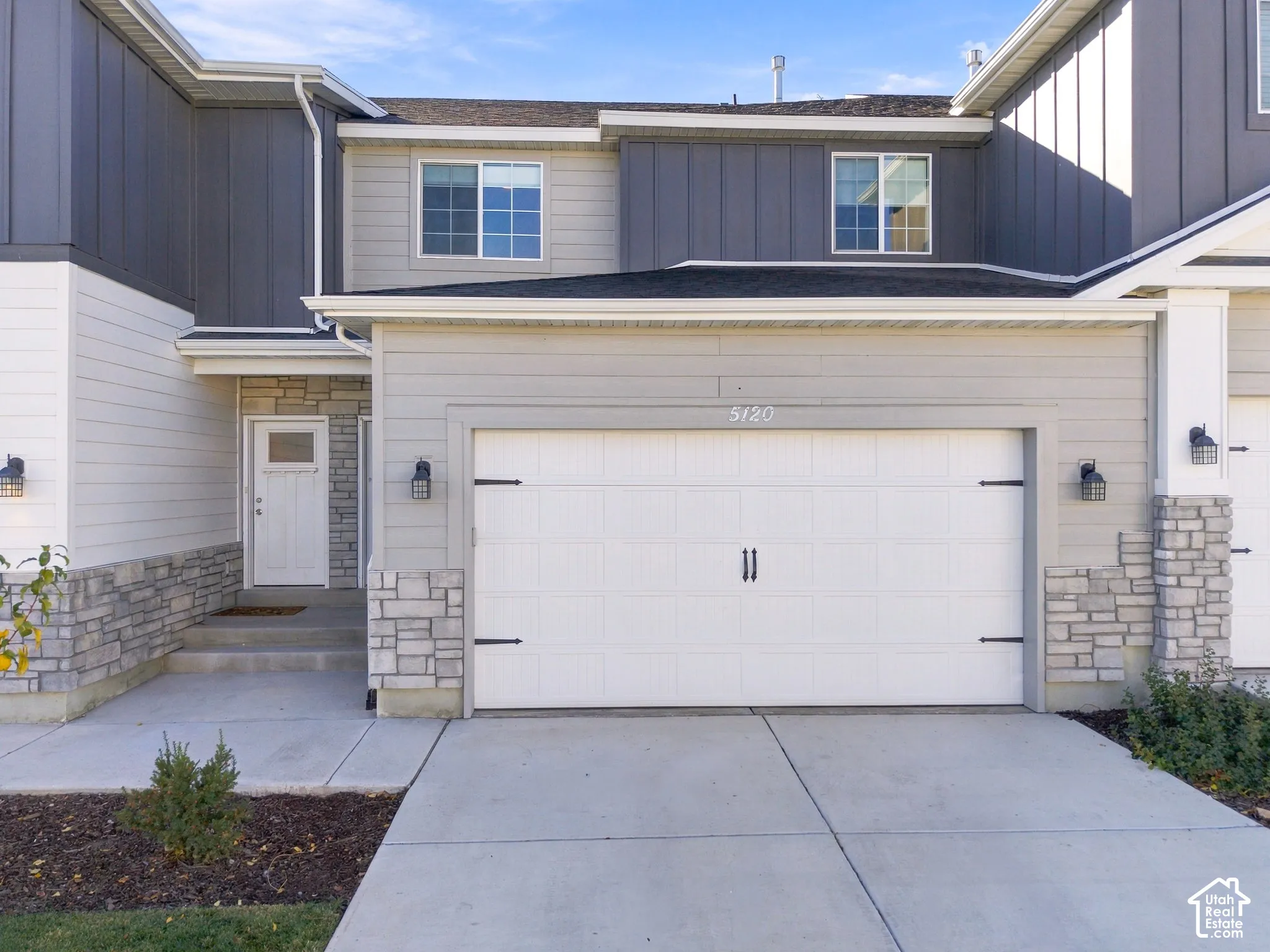 Multi-level exterior featuring a stone veneer foundation, horizontal lap and vertical board-and-batten siding, a single-car garage with decorative hardware, and an integrated covered entryway