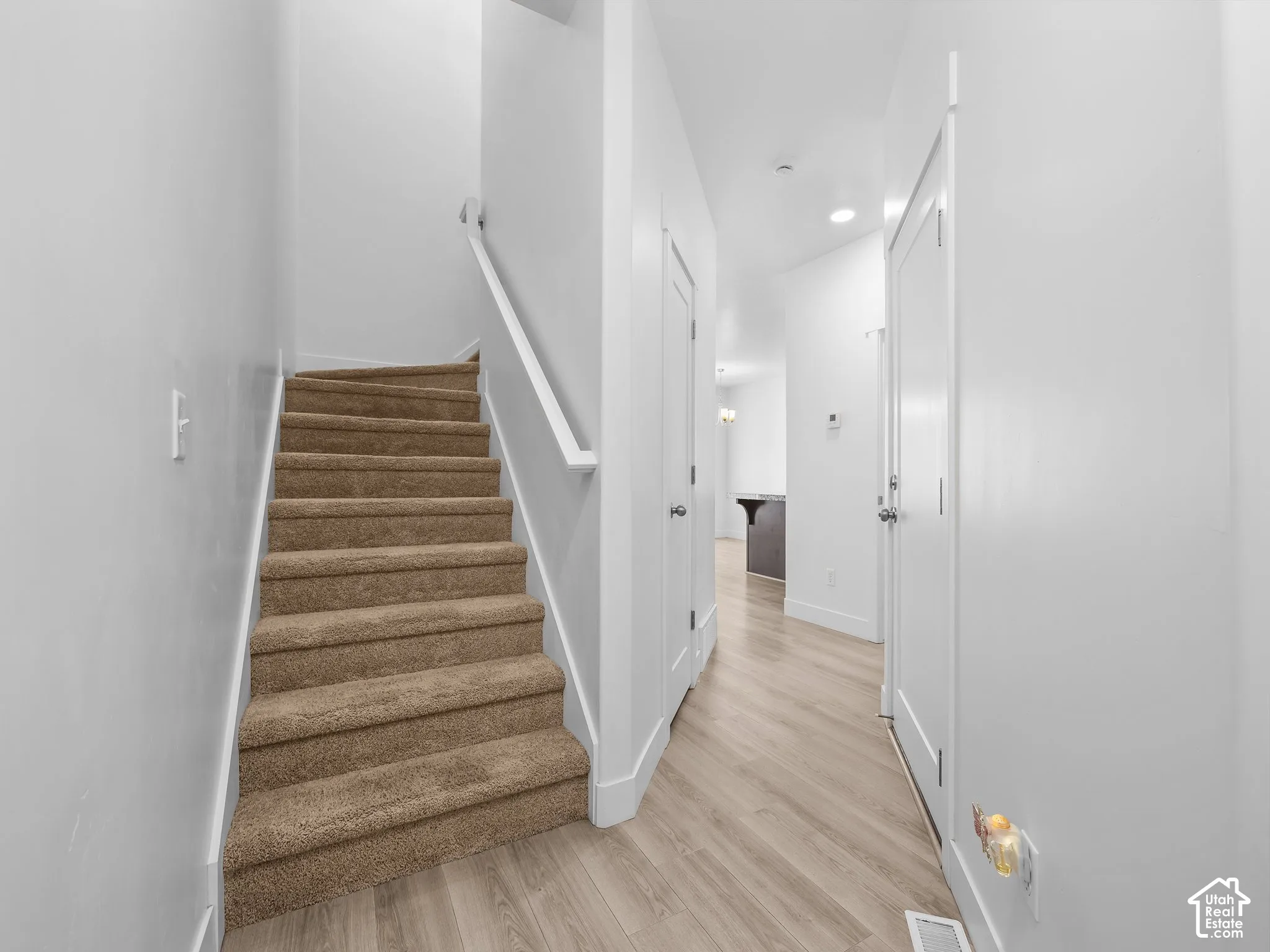 Carpeted staircase featuring a white painted handrail, wood-finish flooring, recessed lighting, and white interior doors