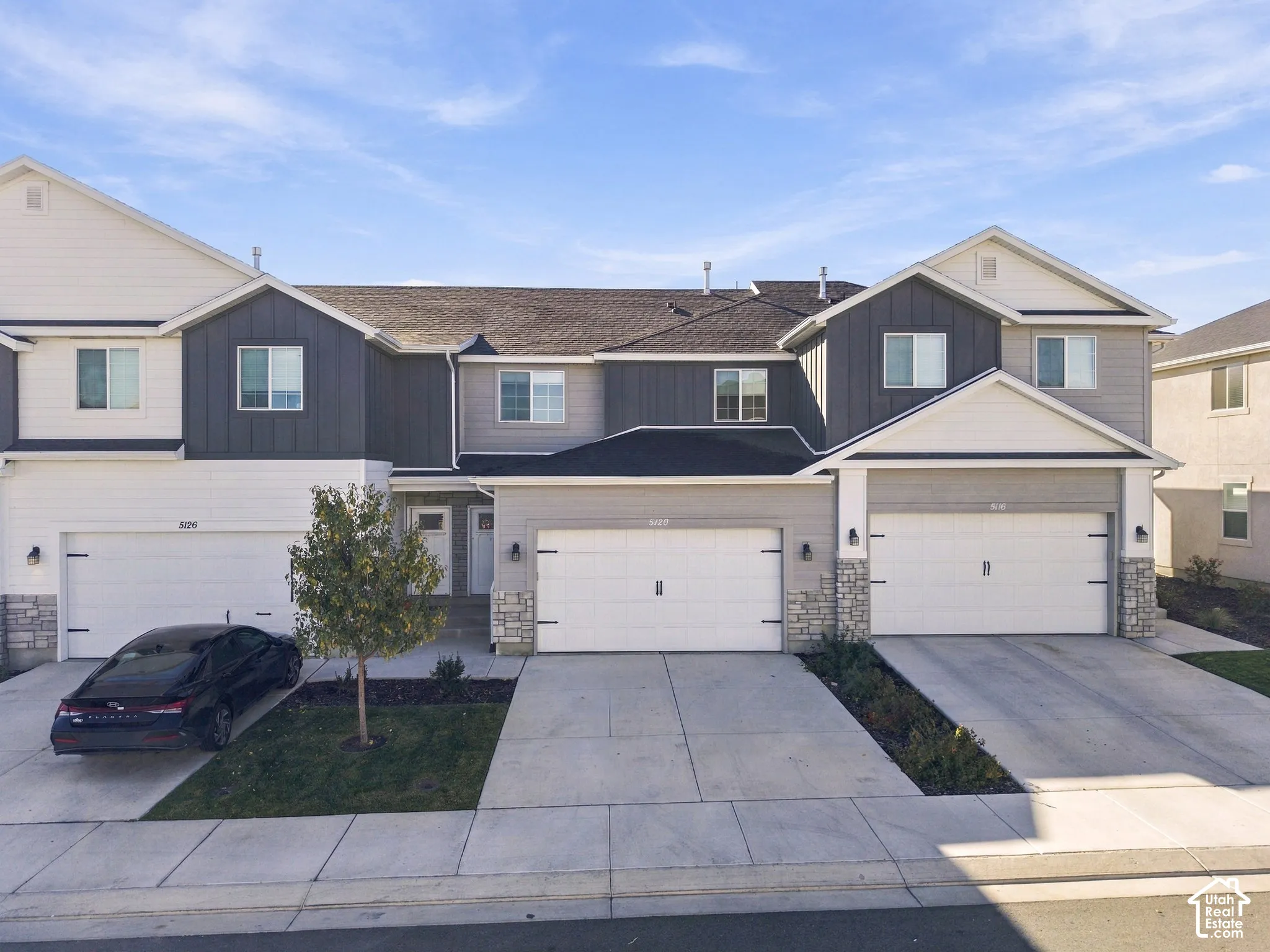 Multi-unit exterior featuring composite vertical siding, stone veneer accents, multi-gabled rooflines, and private attached garages