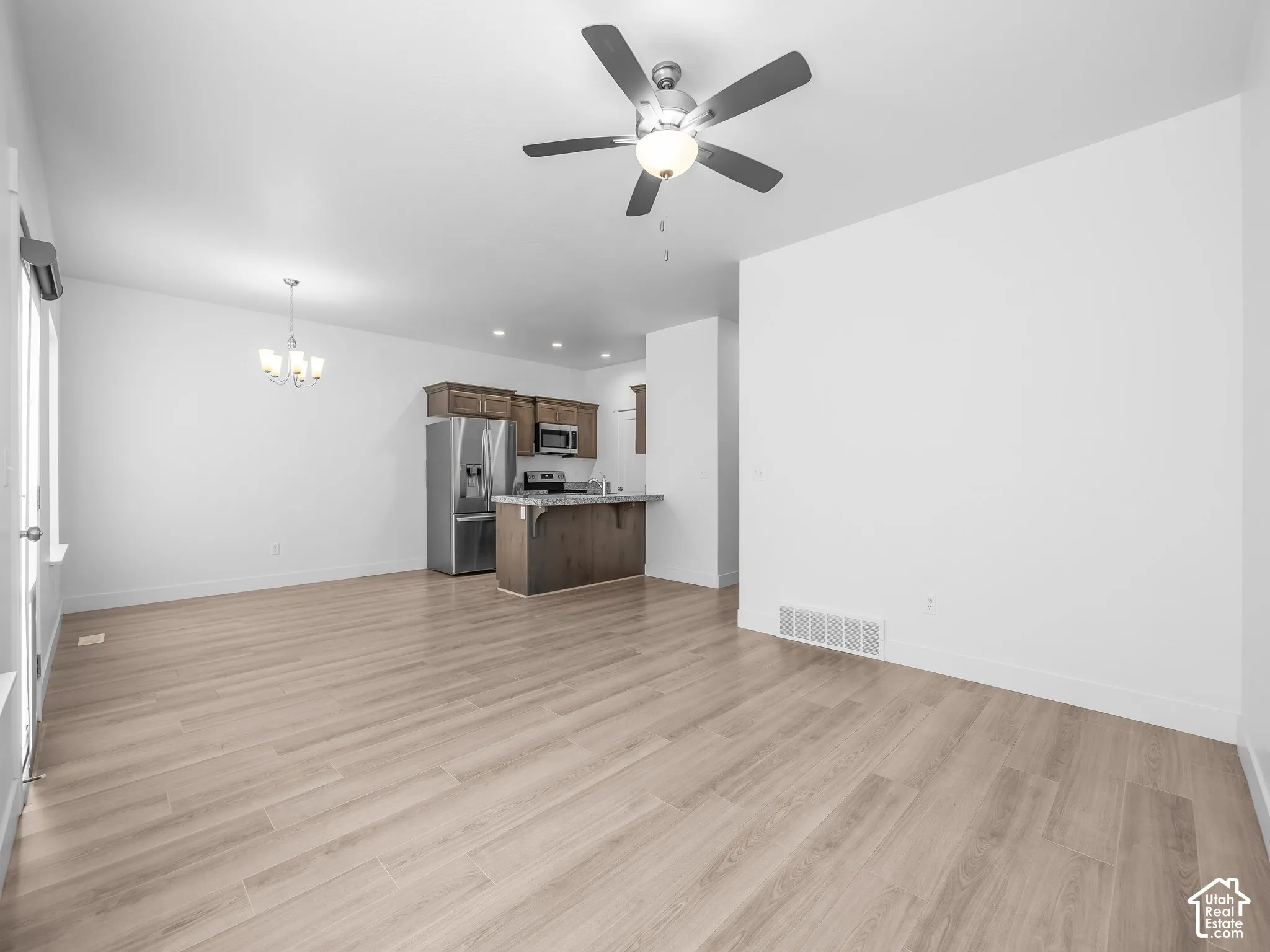 Wood-finish flooring, ceiling fan with integrated light fixture, stainless steel appliances, stained wood cabinetry, and pendant chandelier