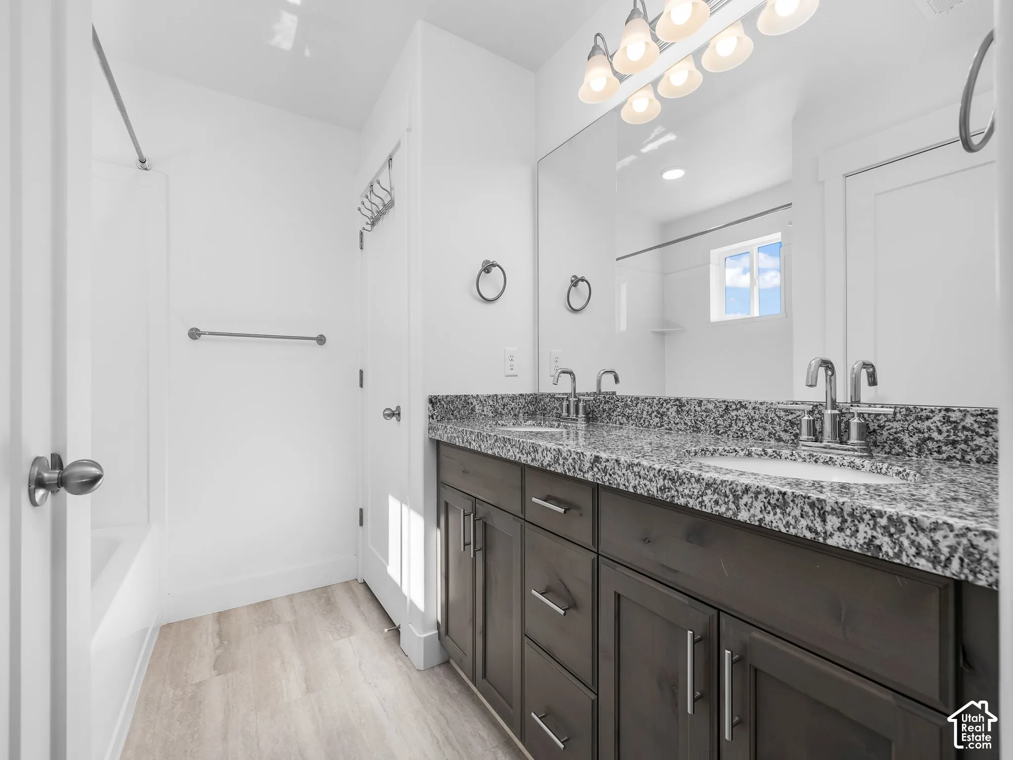 Double vanity with stone-composite countertop, undermount sinks, wood-finish cabinetry, and full-width mirror with multi-light fixture