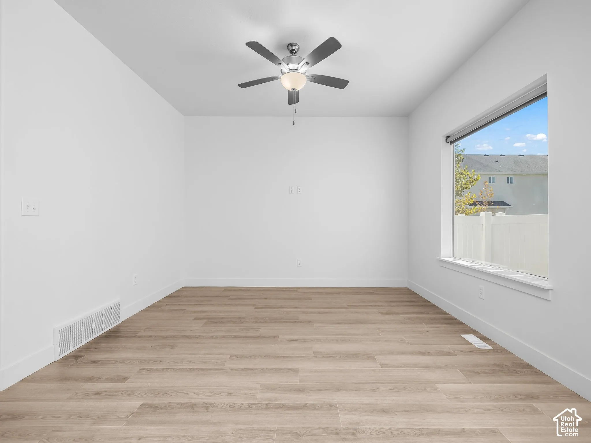 Neutral interior featuring wood-finish flooring, a ceiling fan with integrated lighting, and a large window