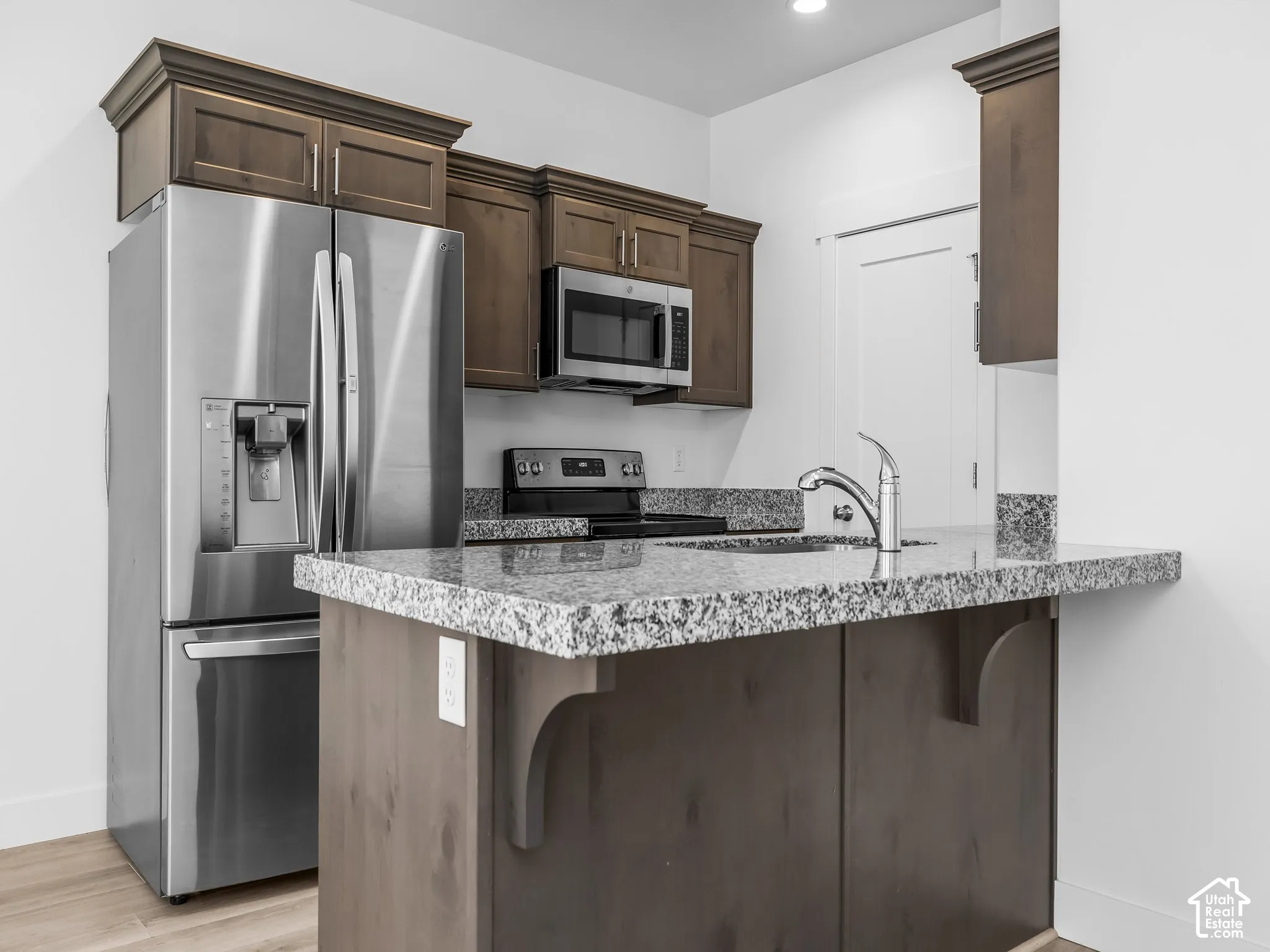 Kitchen featuring dark wood cabinetry, stone countertops, stainless steel refrigerator, built-in microwave, and wood-finish flooring