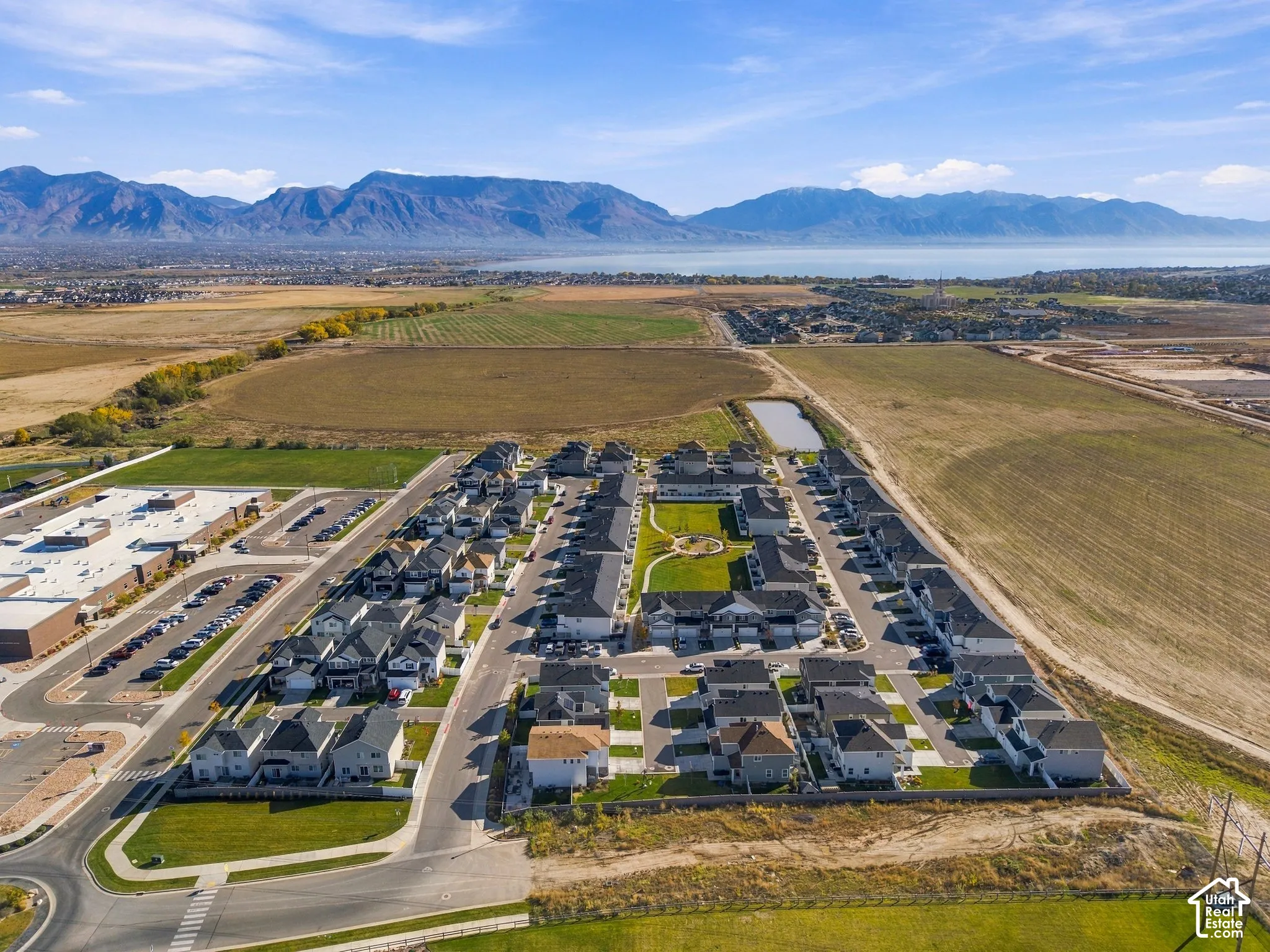 Aerial perspective of a multi-unit residential community featuring asphalt roadways, a central landscaped courtyard with turf, concrete sidewalks, and a prominent mountain range backdrop