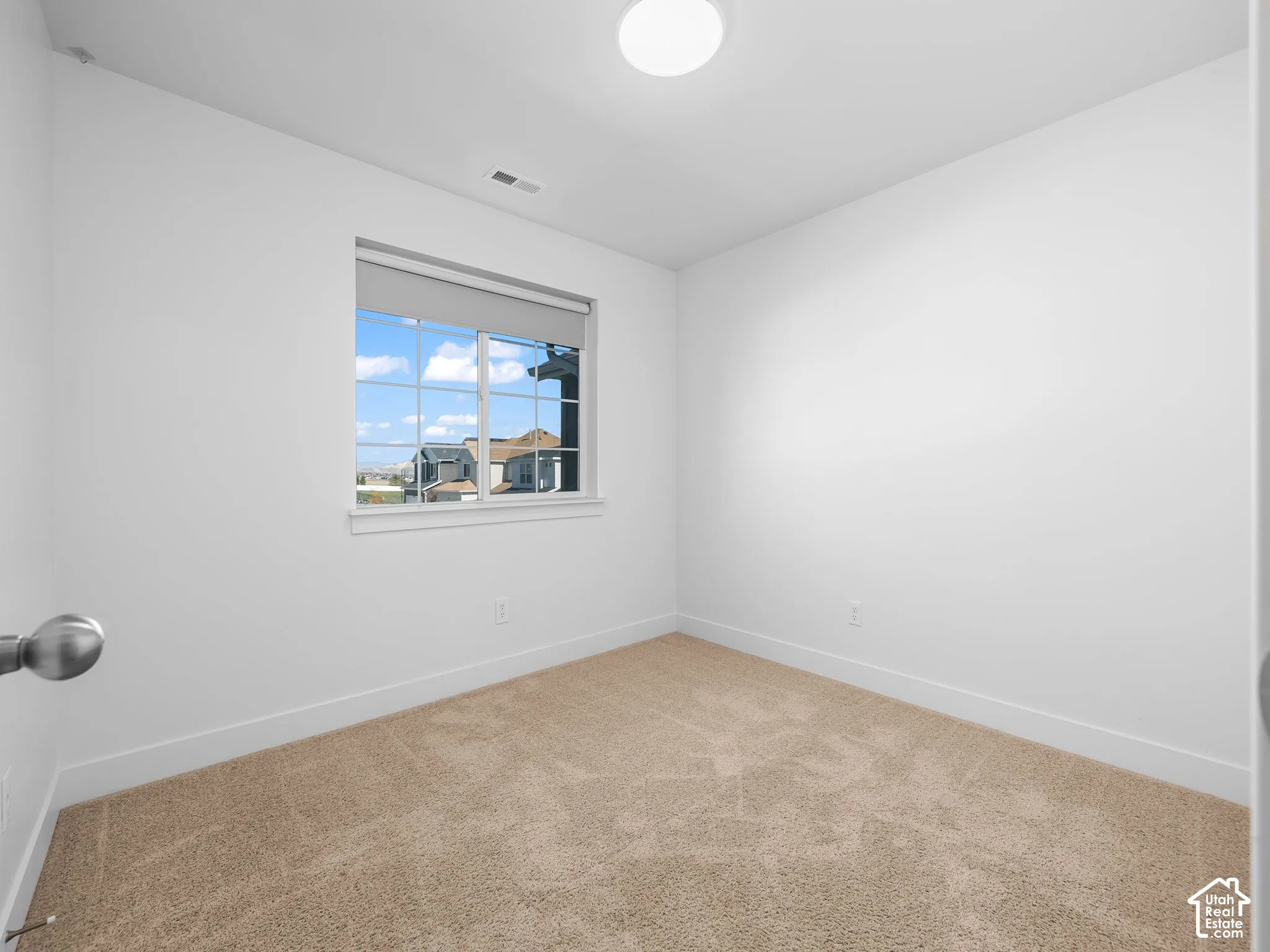 Room featuring neutral-toned carpeting, crisp white walls, and a multi-pane window with a roller shade