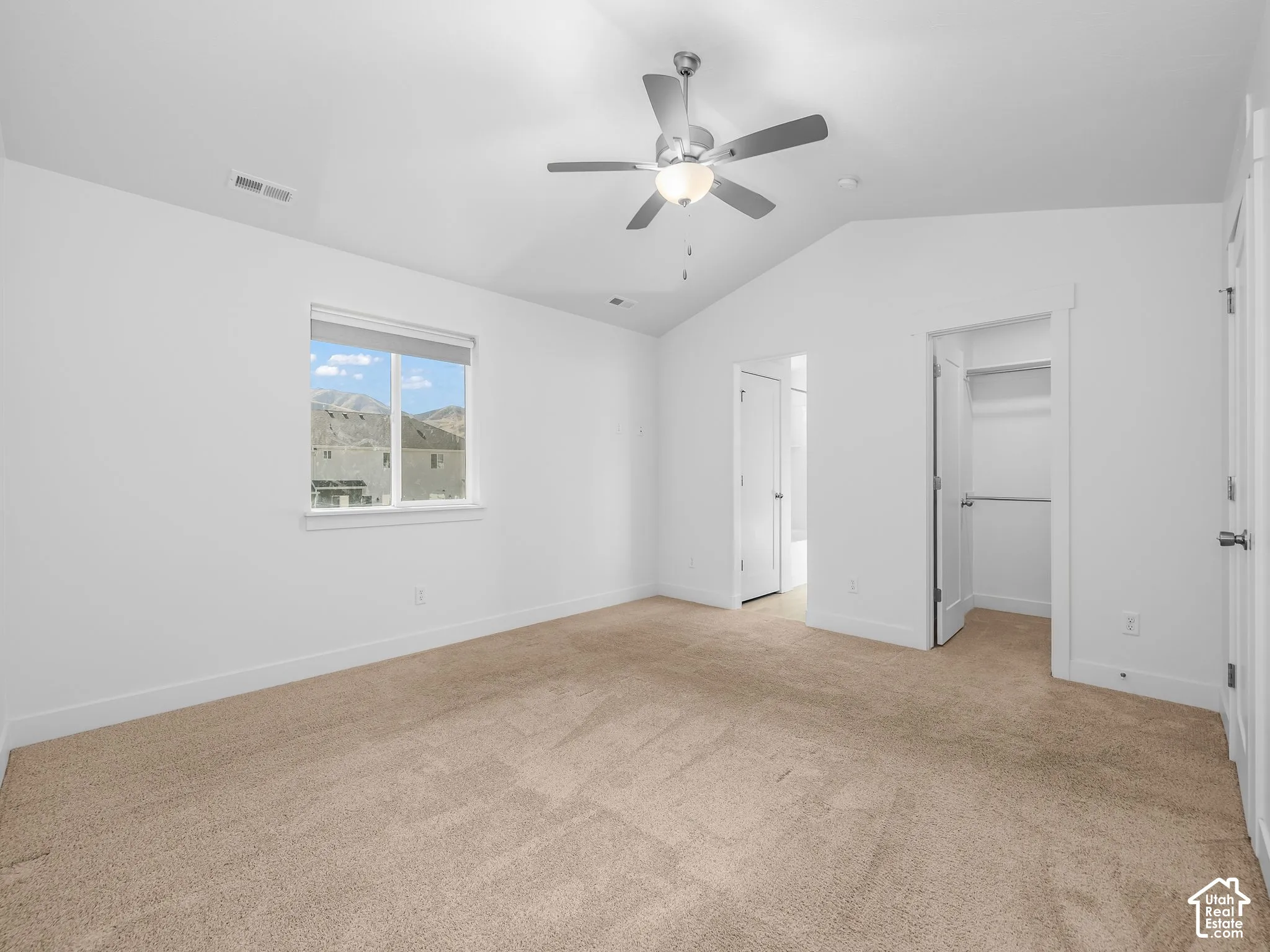 Vaulted ceilings, neutral carpeting, a central ceiling fan with integrated lighting, and a walk-in closet
