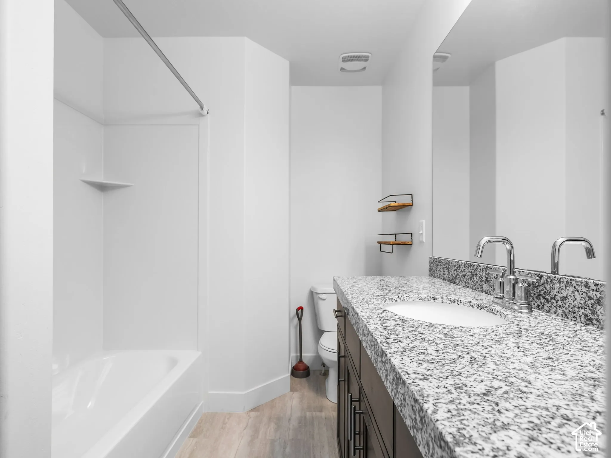 Bathroom featuring a vanity with a stone-finish countertop, undermount sink, dark-toned cabinetry, and wood-finish flooring, accompanied by a full-length wall mirror and a tub-shower combination