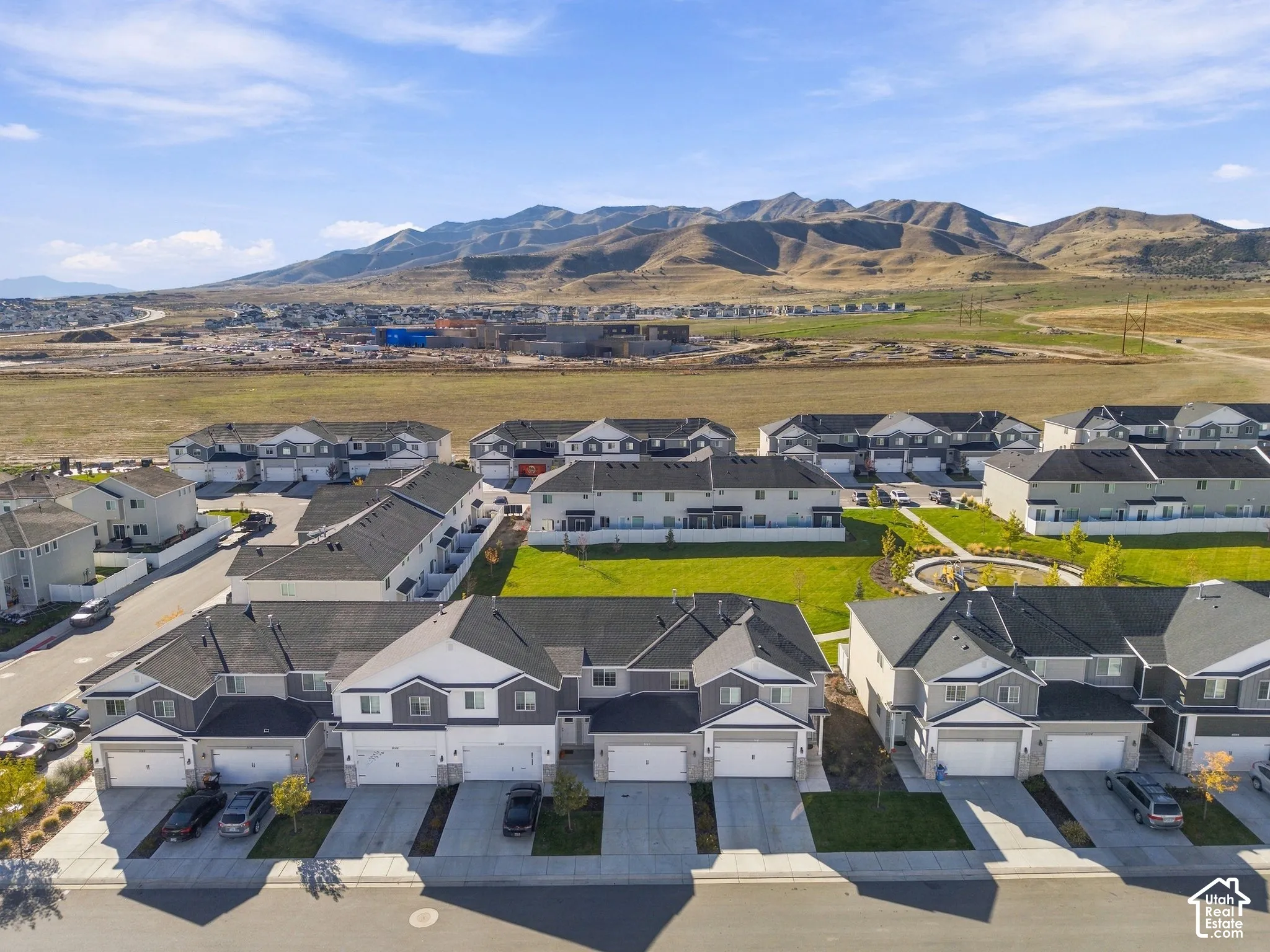 Aerial perspective of multi-family residences featuring attached garages, concrete driveways, communal green space, and mountain backdrop