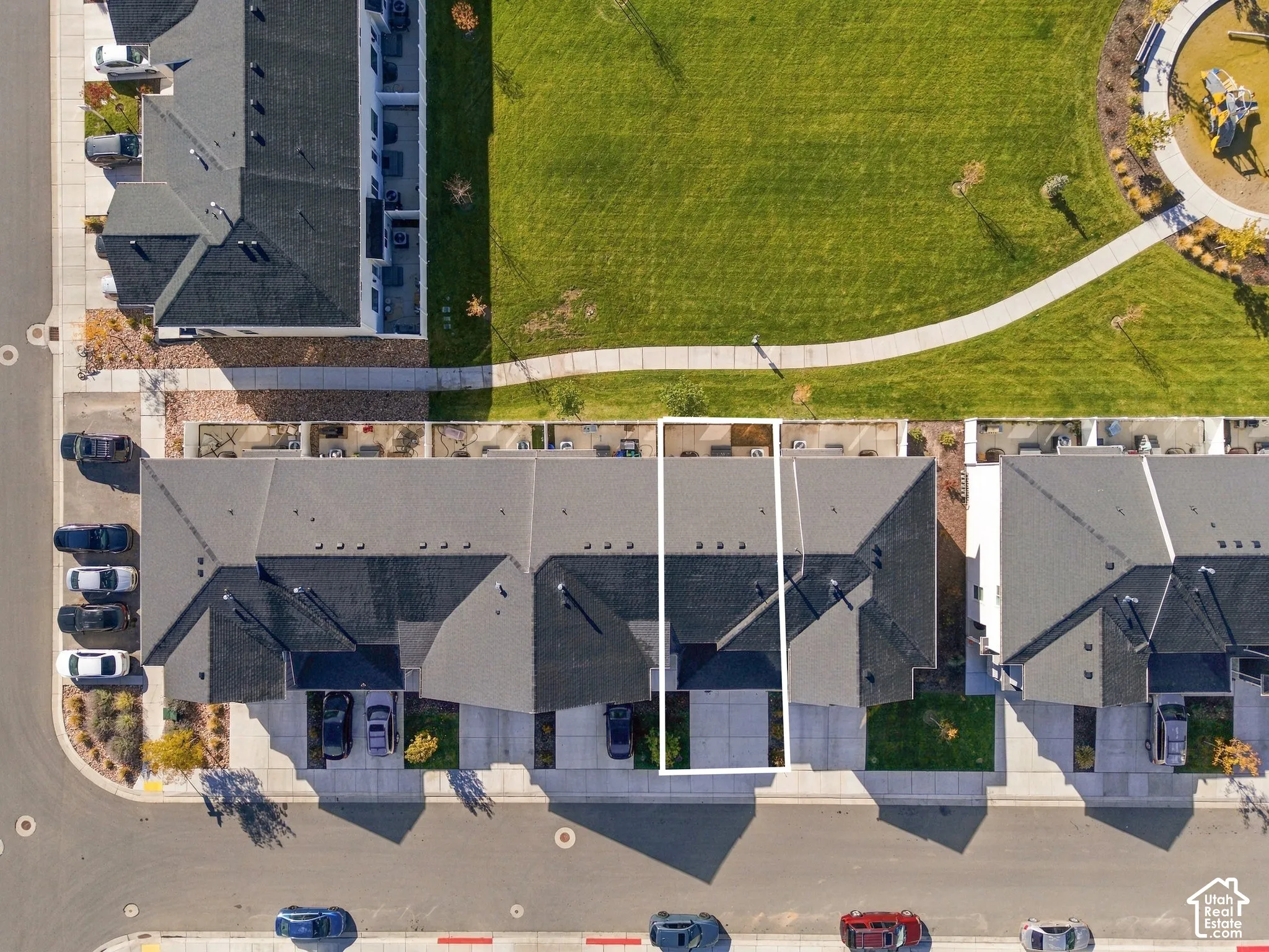 Aerial perspective of property featuring a concrete driveway, multi-gabled asphalt shingle roof, rear concrete patio, and immediate proximity to an expansive green space with a paved walking path