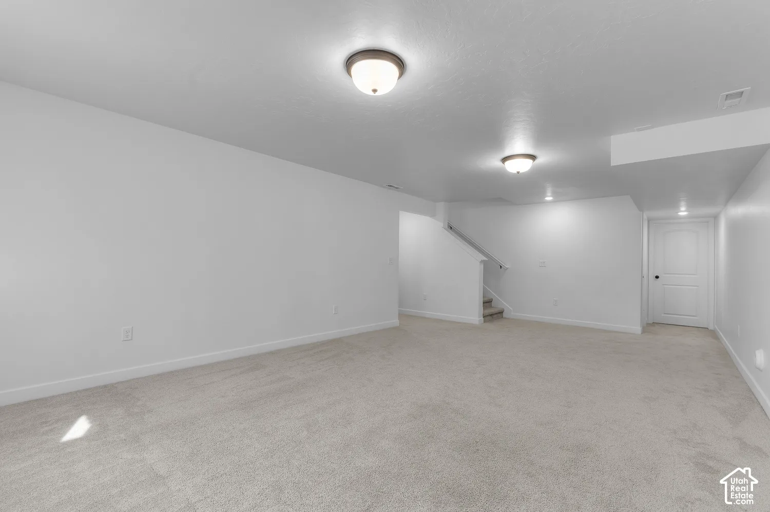 Neutral-toned carpeting, two flush-mount ceiling light fixtures, white walls, and a multi-panel interior door