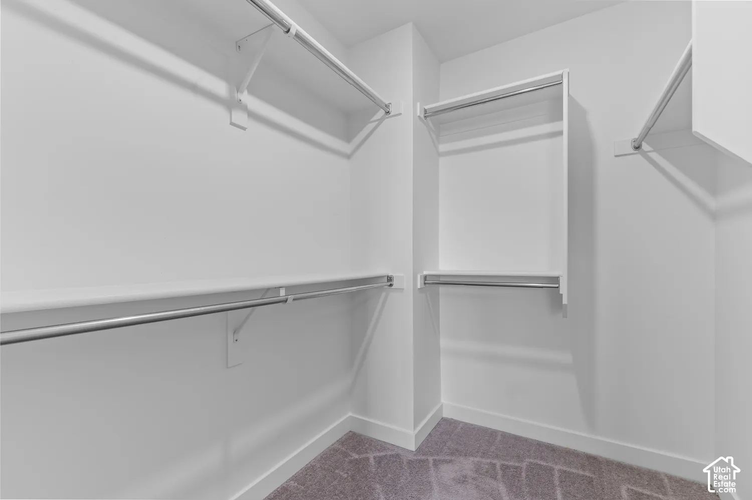 Walk-in closet featuring tiered white shelving and integrated metal garment rods