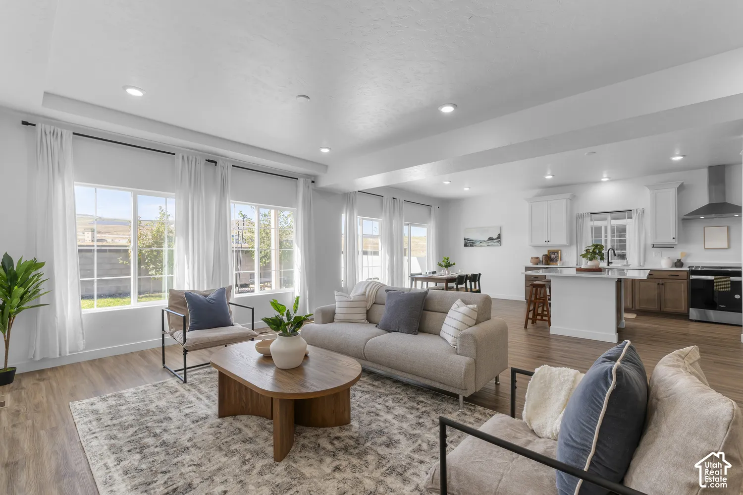 Open-concept living space featuring wood-finish flooring, recessed lighting, expansive multi-pane windows, and a kitchen equipped with a center island and stainless steel range hood
