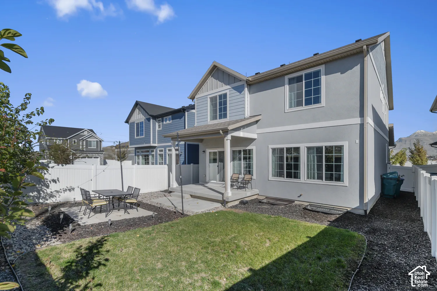 Rear exterior featuring a two-story light gray facade, covered concrete patio, enclosed backyard with a vinyl privacy fence, and a manicured lawn