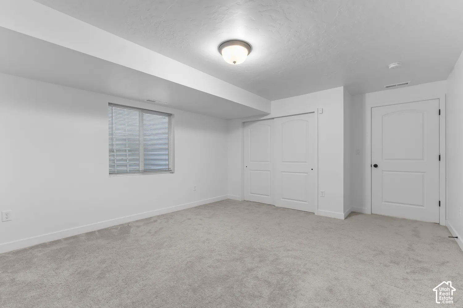 Neutral-toned carpeting, sliding double-door closet, solid-core panel door, flush-mount ceiling lighting, and window with built-in blinds