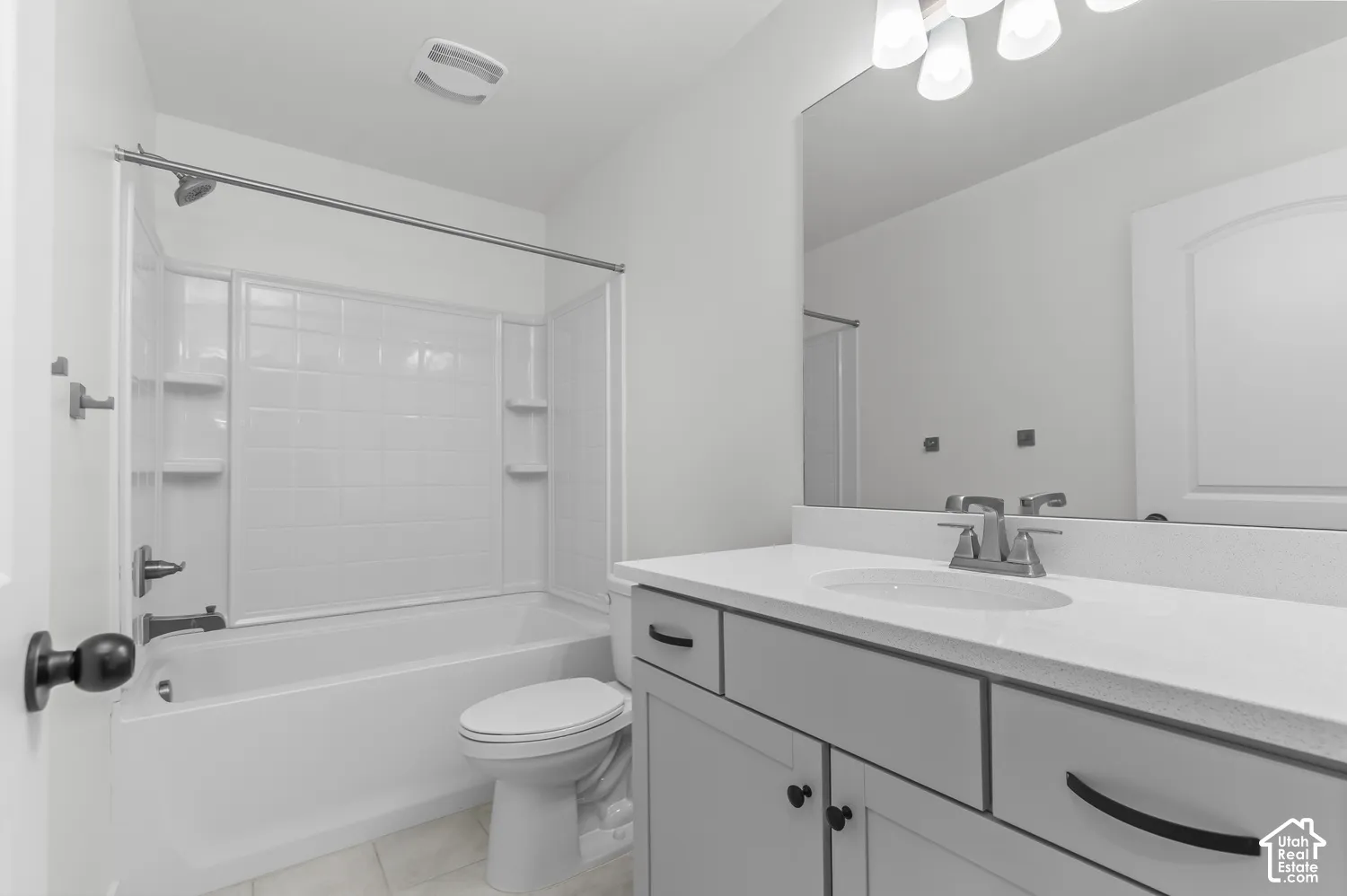 Bathroom featuring a vanity with a light-toned countertop, integrated basin, matte black hardware, a large wall-mounted mirror, and a tub-shower combination with built-in shelving