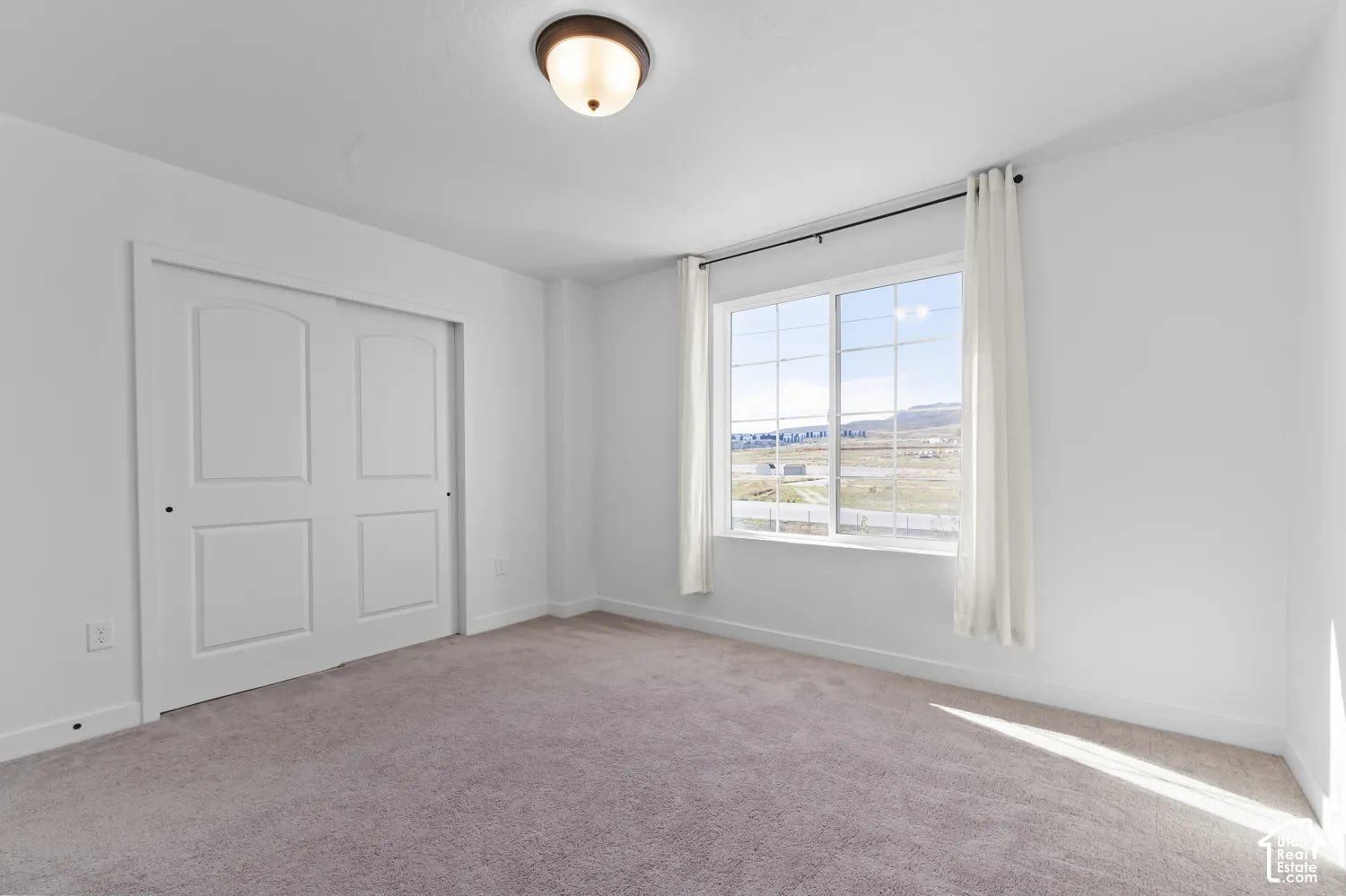 Neutral interior space featuring carpeted flooring, two-panel sliding closet doors, a multi-pane window with mountain scenery, and a central flush-mount light fixture