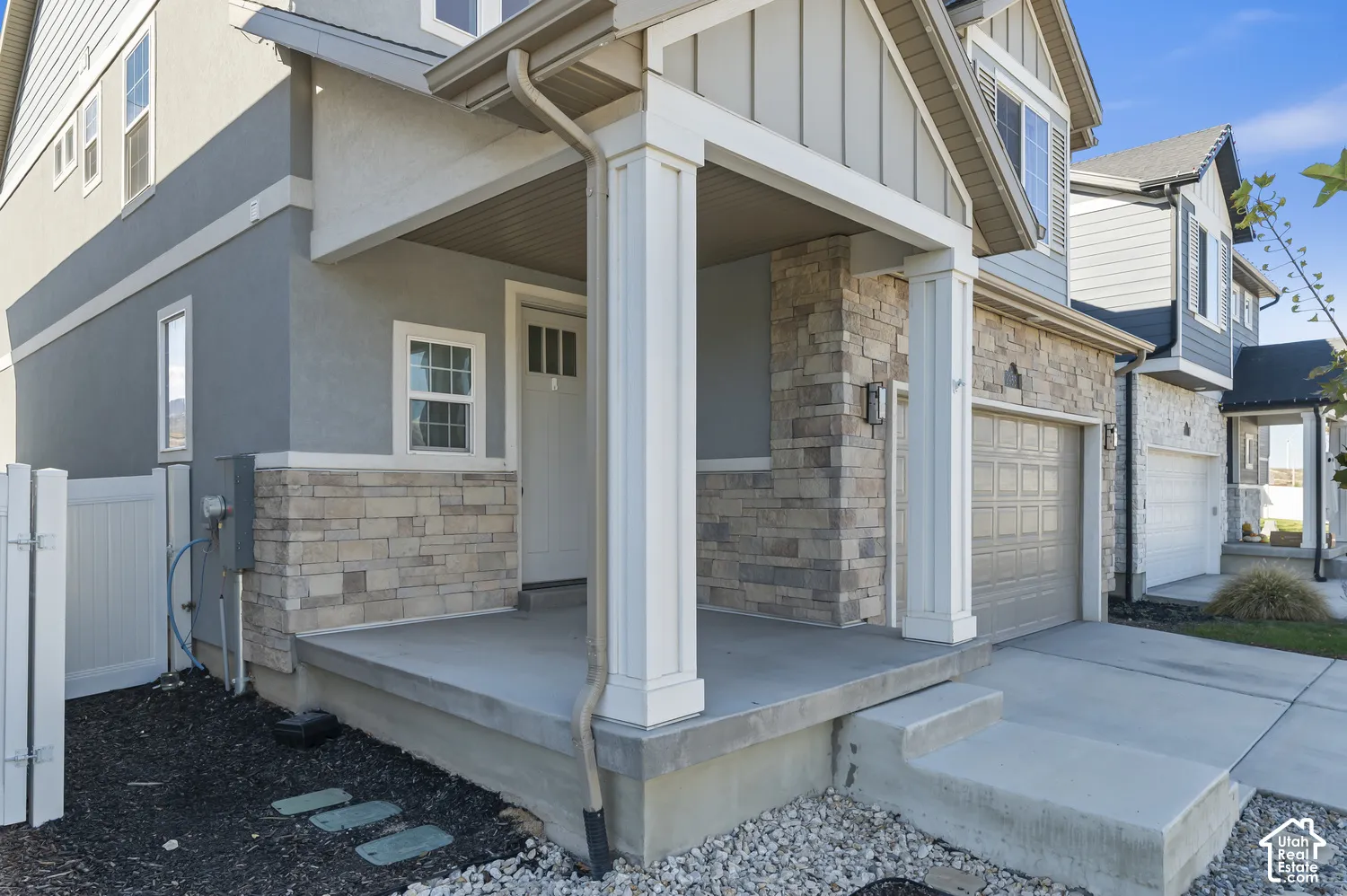 Exterior facade featuring a combination of stucco and stacked stone veneer, a covered concrete front porch with square columns, and a multi-paneled garage door