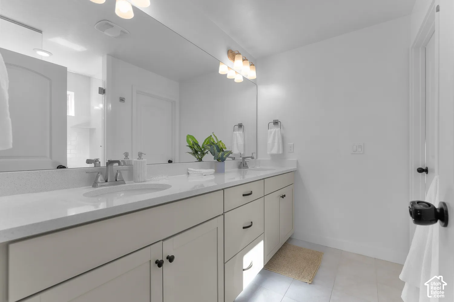 Bathroom featuring a dual-sink vanity with light-toned cabinetry, solid-surface countertops, large wall-spanning mirror, and chrome fixtures