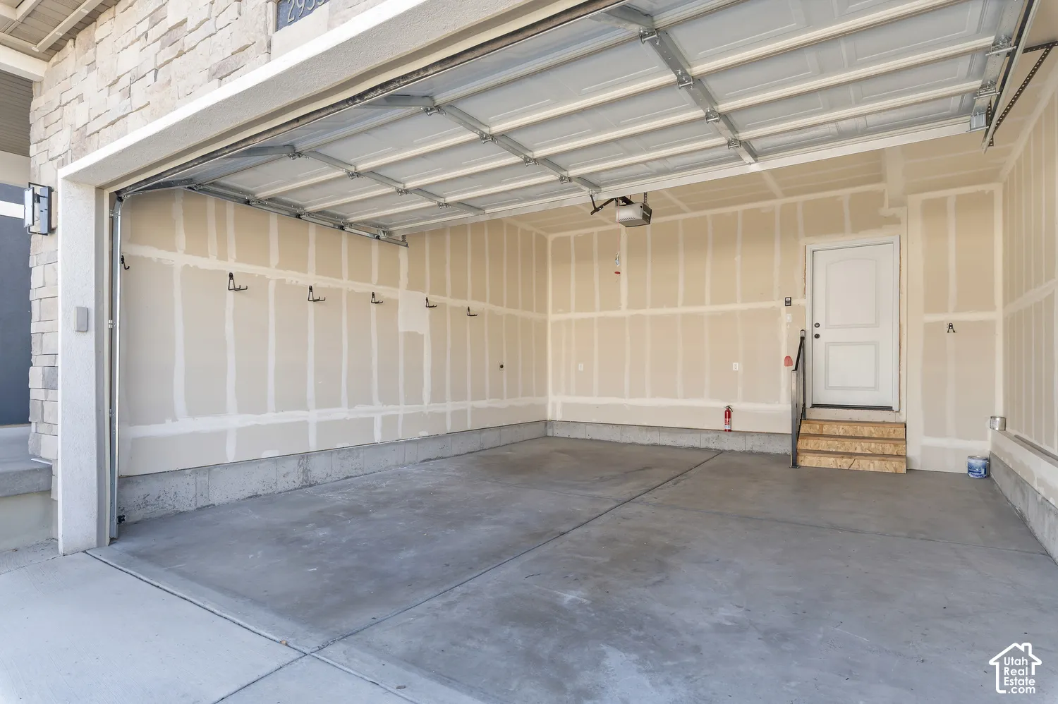 Two-car garage featuring a concrete floor, finished drywall, overhead garage door system, and an elevated side entry door with wood-tread stairs