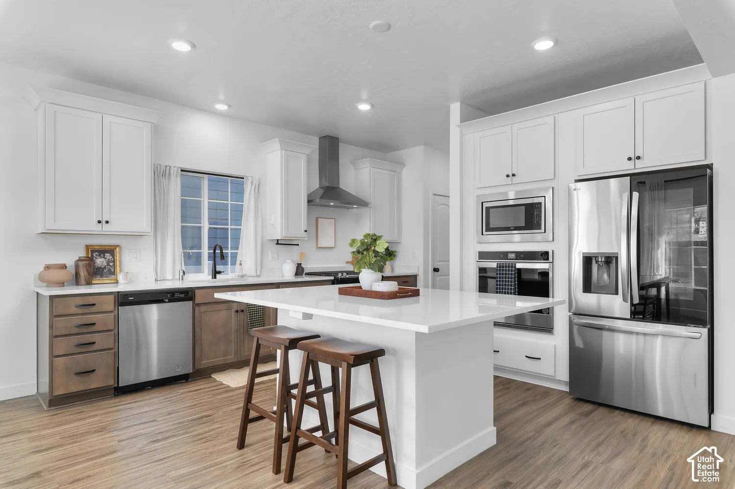 Kitchen featuring a center island with a white countertop, two-tone cabinetry, stainless steel appliances, and wood-finish flooring