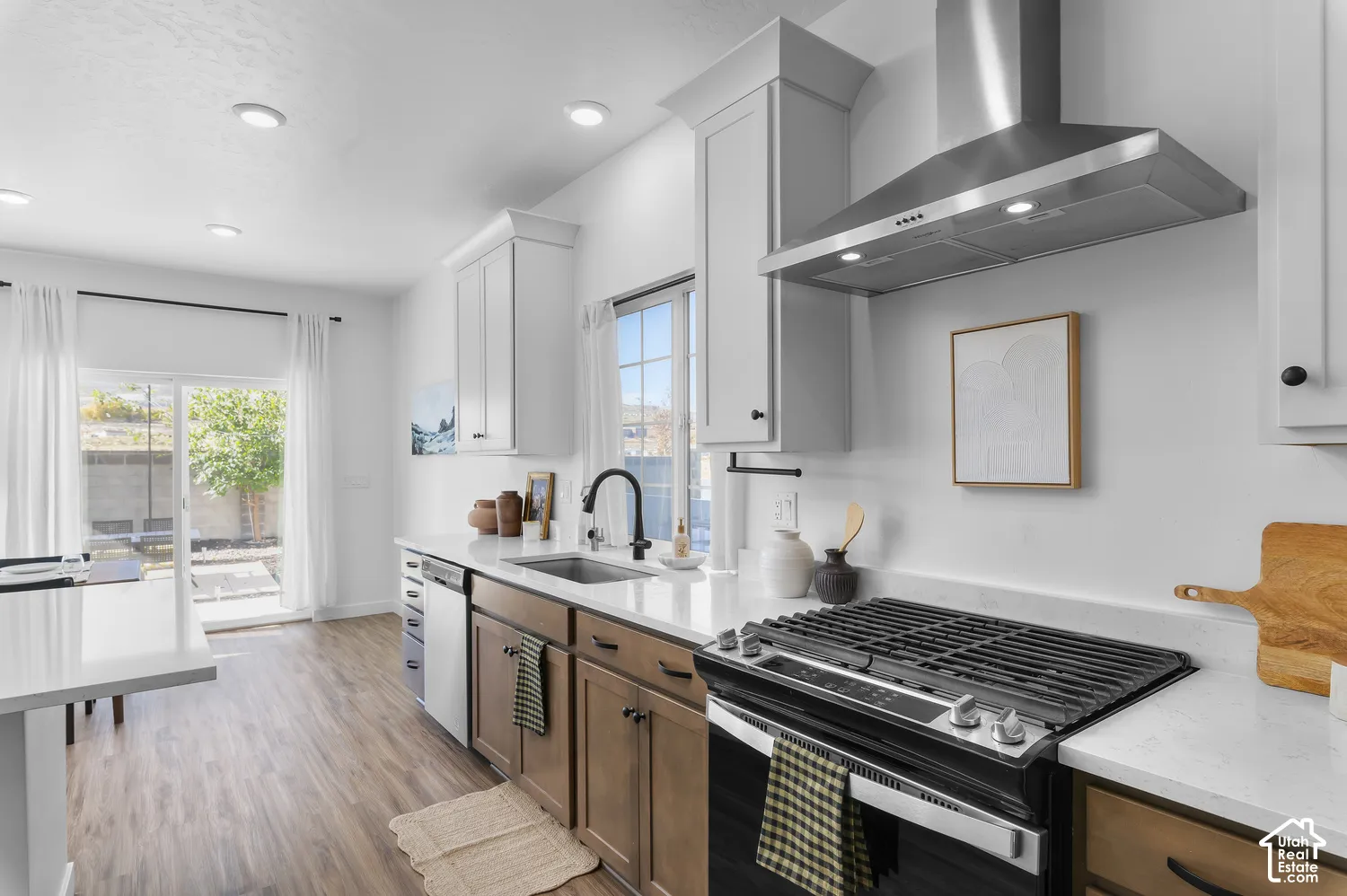 Kitchen featuring wood-finish cabinetry, white countertops, stainless steel gas range, stainless steel range hood, and wood-finish flooring