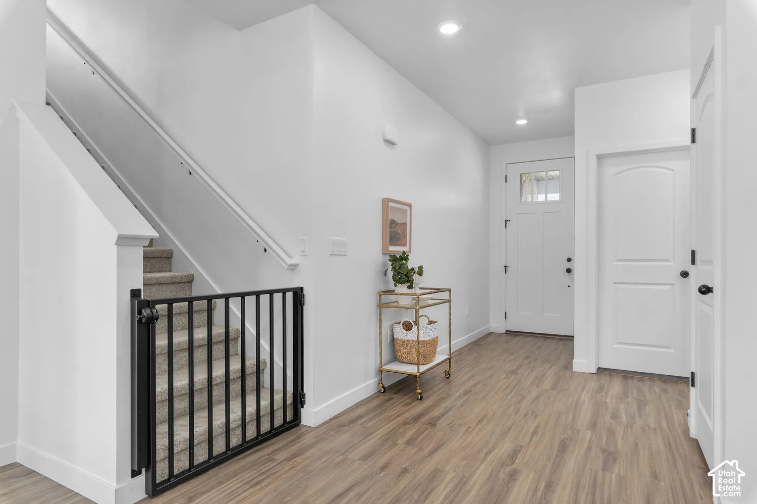 Entryway featuring wood-finish flooring, recessed lighting, carpeted staircase with white handrail, and a white front door with an integrated glass pane