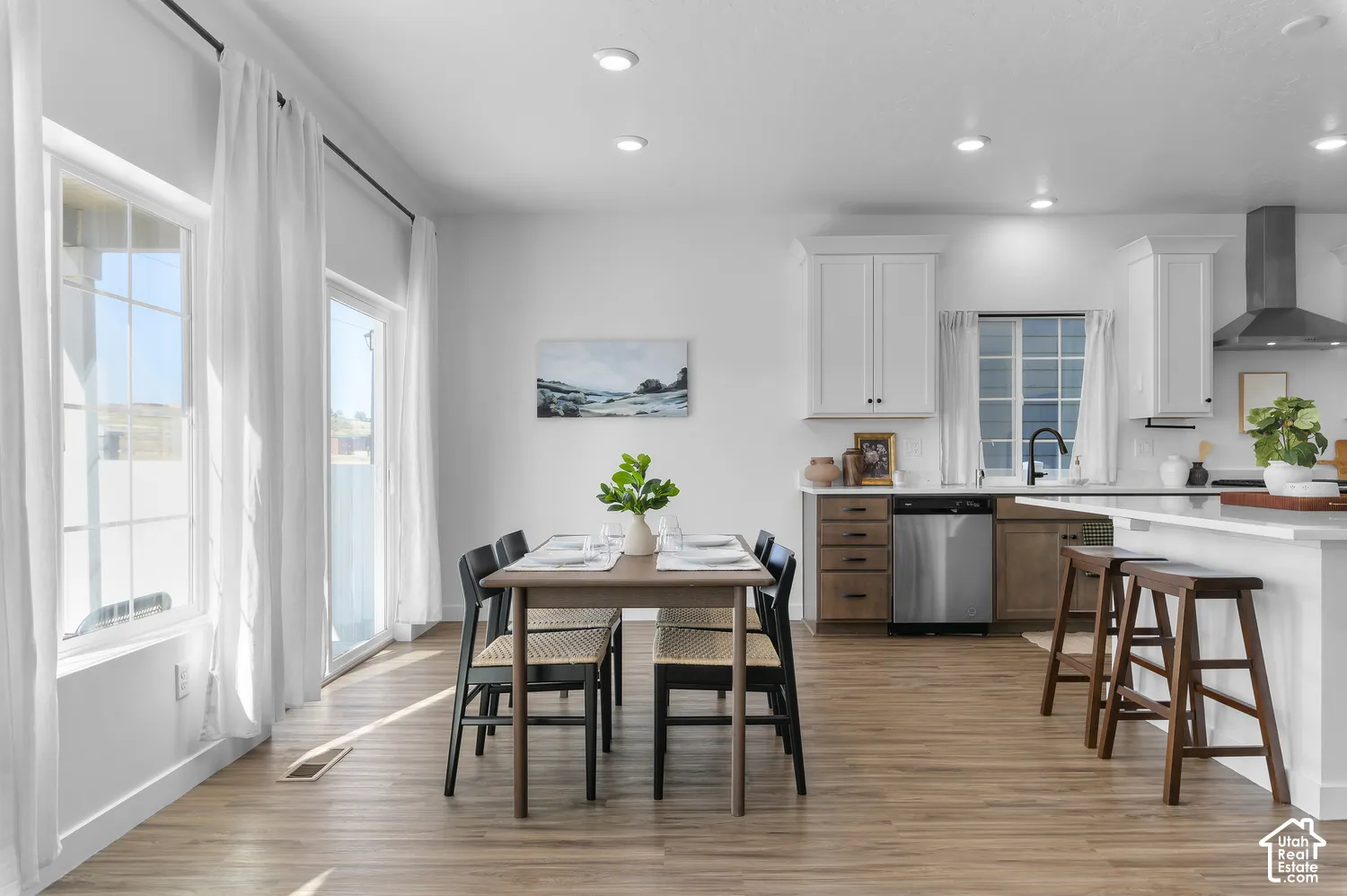 Kitchen area featuring white upper cabinetry, two-tone lower cabinetry, stainless steel dishwasher, a central island with quartz countertops, and wood-finish flooring