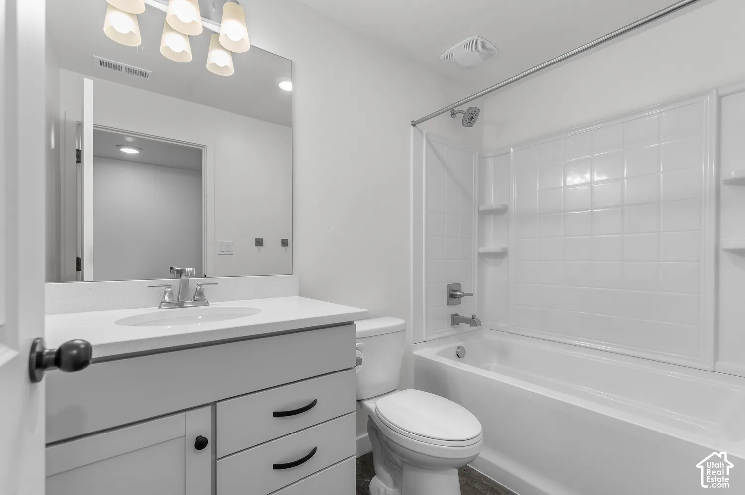 Bathroom featuring a vanity with white countertop, integrated sink, and matte black hardware, paired with a white tub-shower surround and multi-bulb vanity lighting