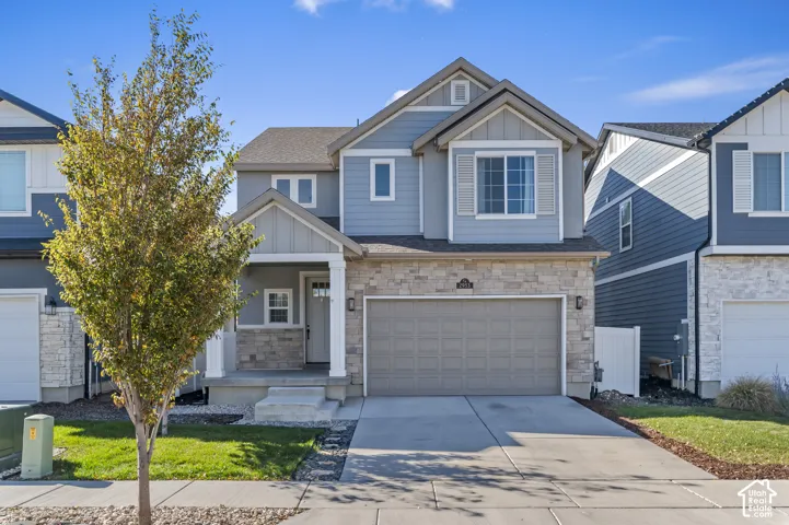 Two-story exterior featuring a mix of horizontal lap siding and board-and-batten siding, stone veneer accents, a covered front porch with a square column, and a concrete driveway