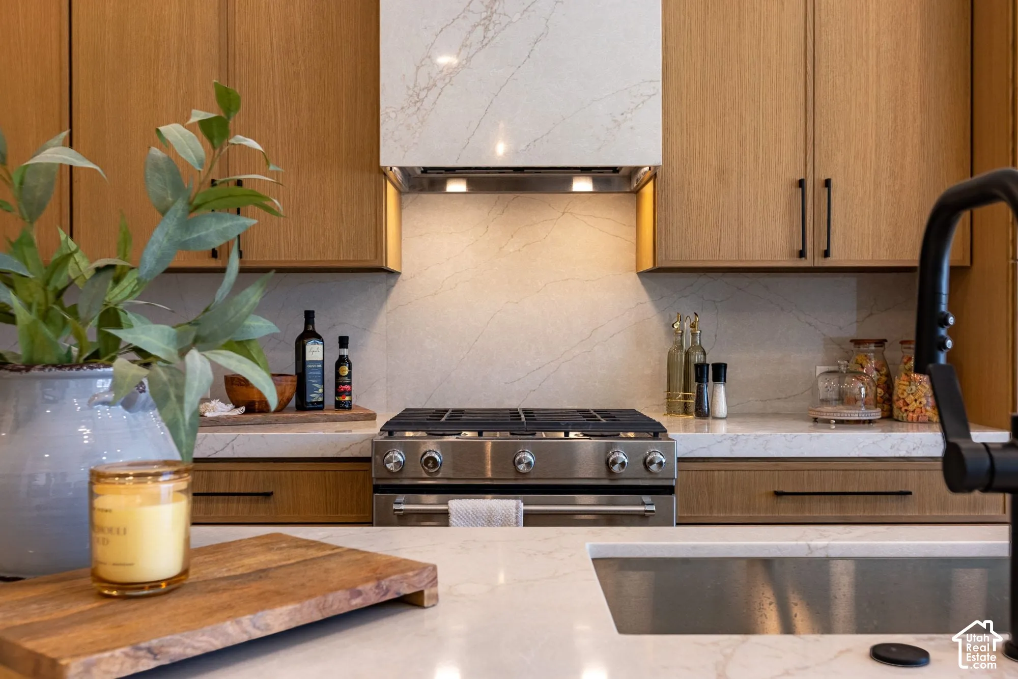 Kitchen featuring flat-panel wood-finish cabinetry, stone-surface countertops with matching backsplash, stainless steel gas range, integrated range hood, and matte black hardware