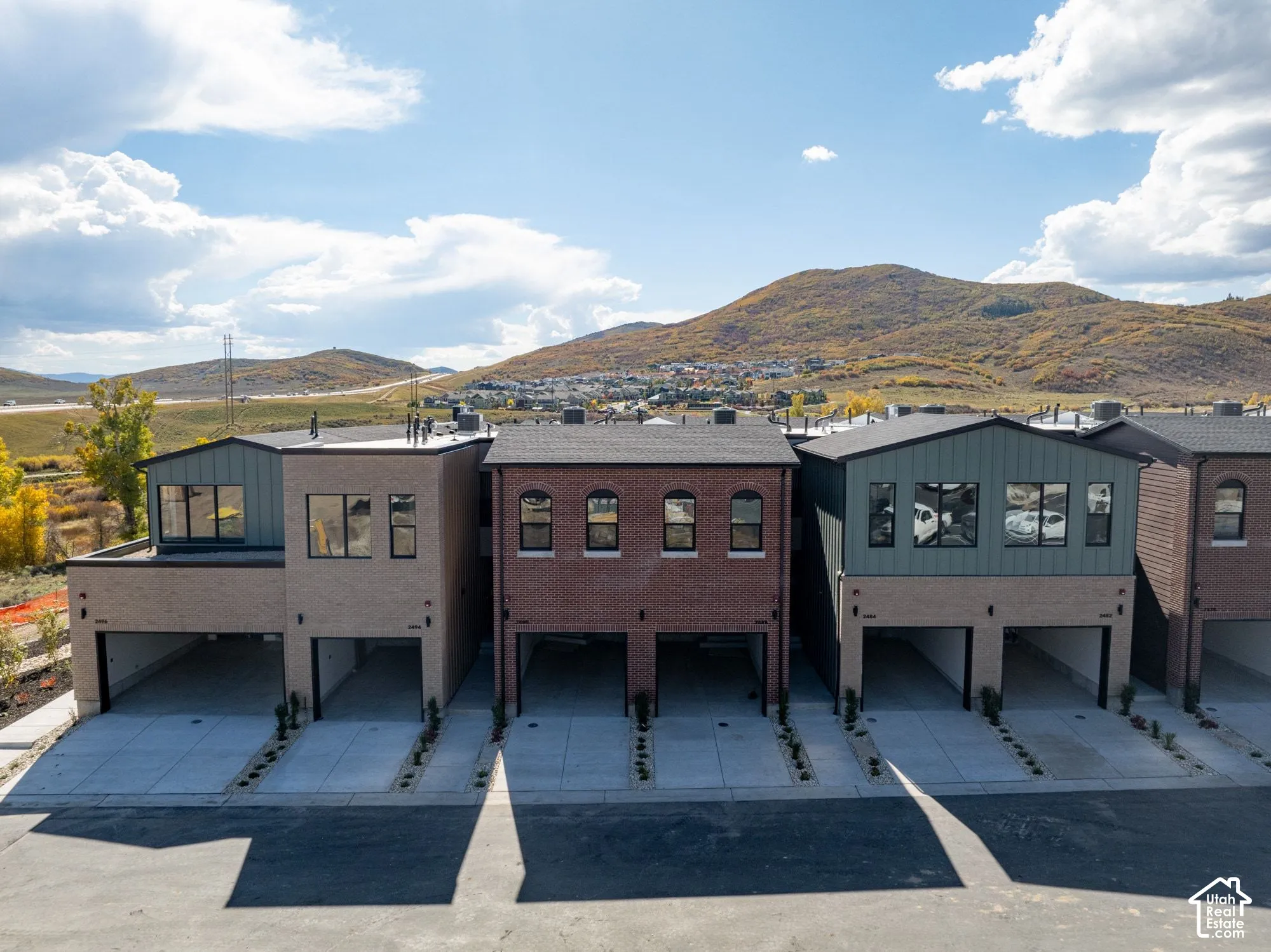 Multi-level exterior featuring brick and metal siding, arched window detailing, and integrated ground-level garage bays set against a mountain backdrop