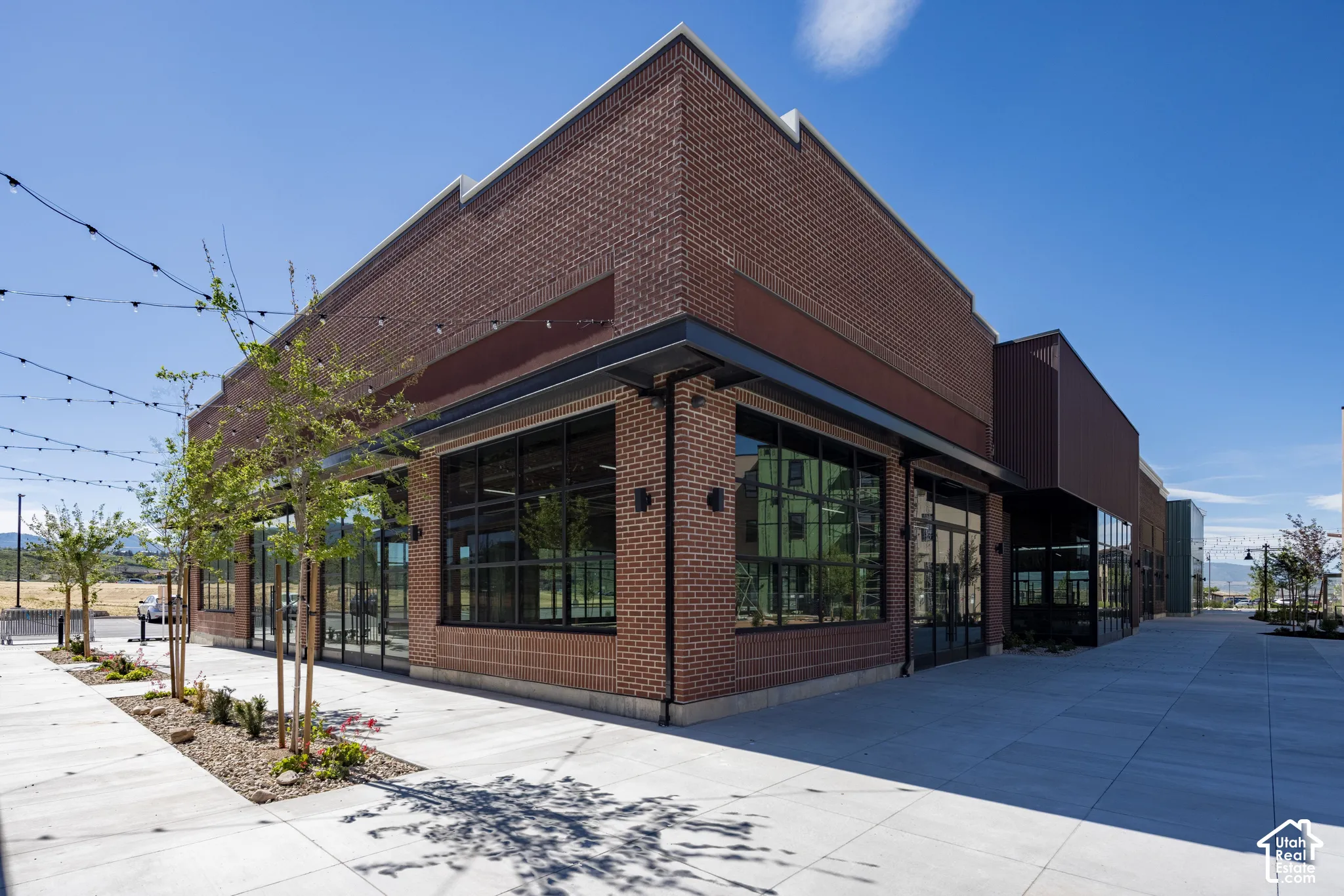 Commercial exterior featuring red brick masonry, expansive floor-to-ceiling windows, black metal framing, and a concrete pedestrian walkway
