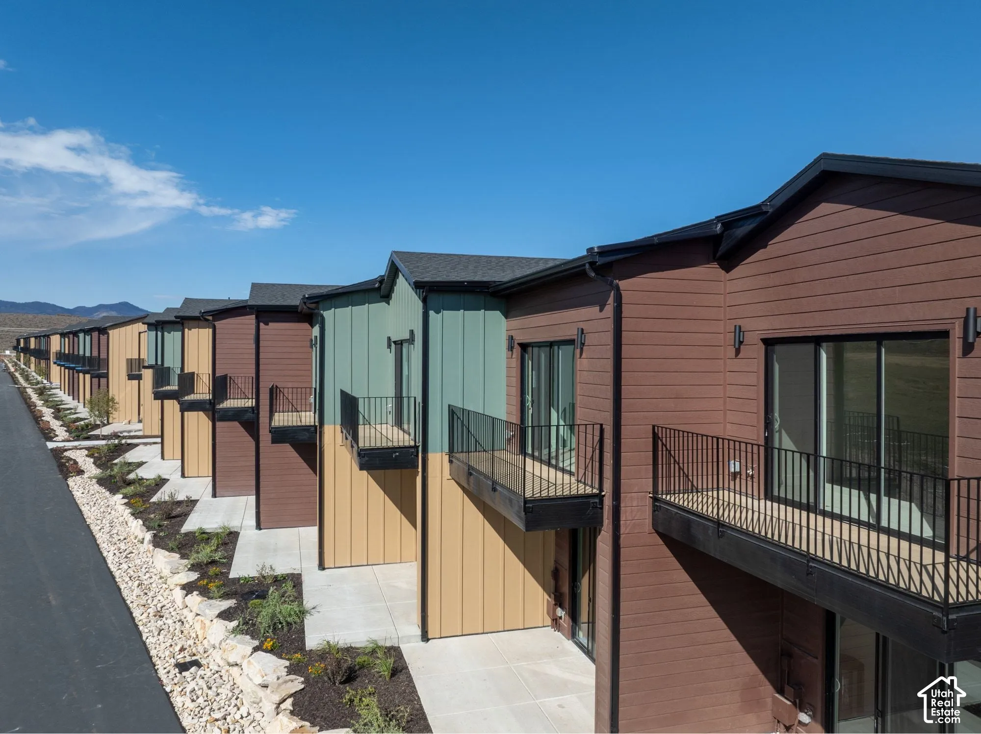 Multi-story exterior featuring multi-toned horizontal lap and vertical board-and-batten siding, private elevated balconies with black metal railings, and concrete ground-level patios