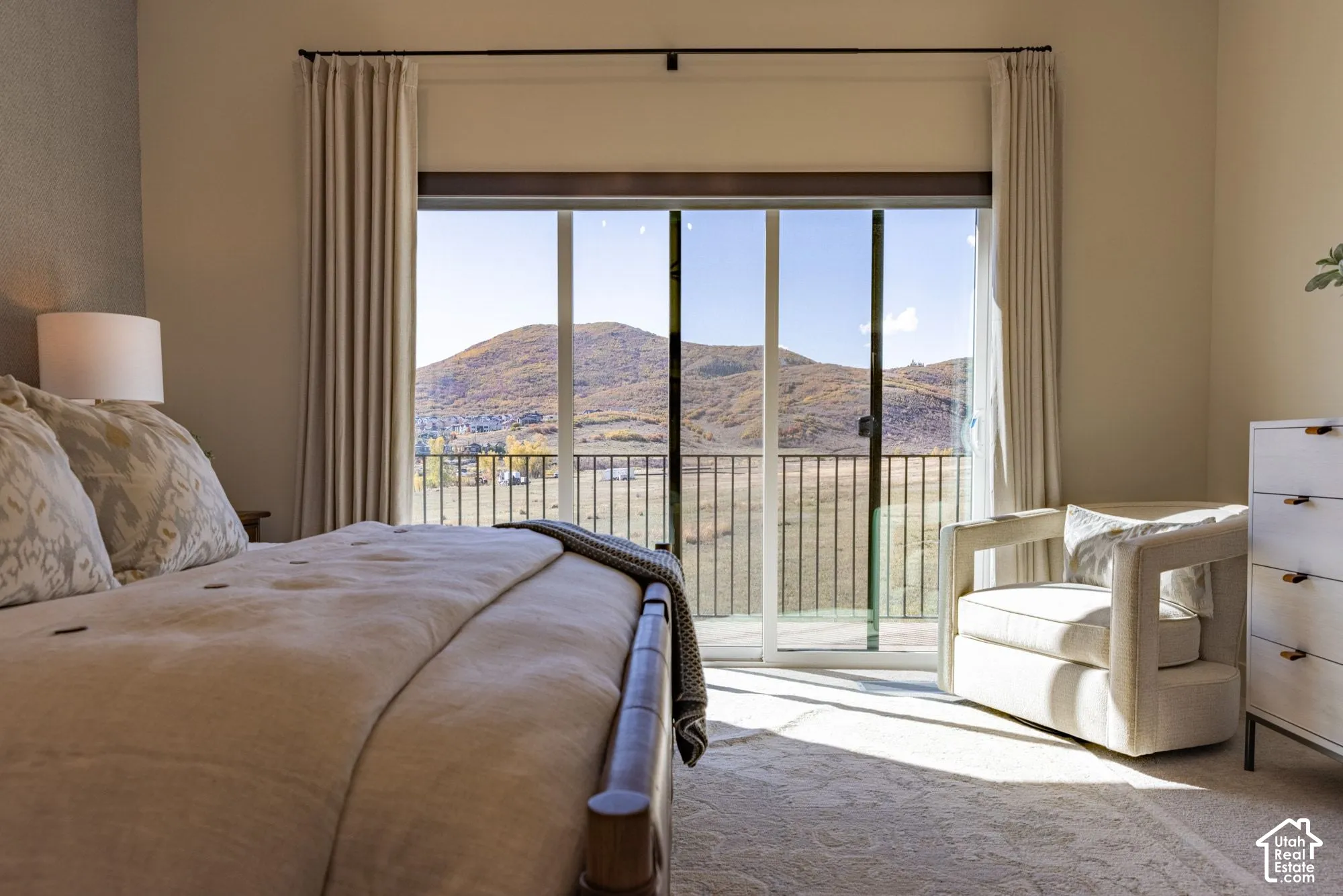 Floor-to-ceiling glass sliding doors opening to a balcony with metal railing, showcasing mountain scenery and neutral wall tones