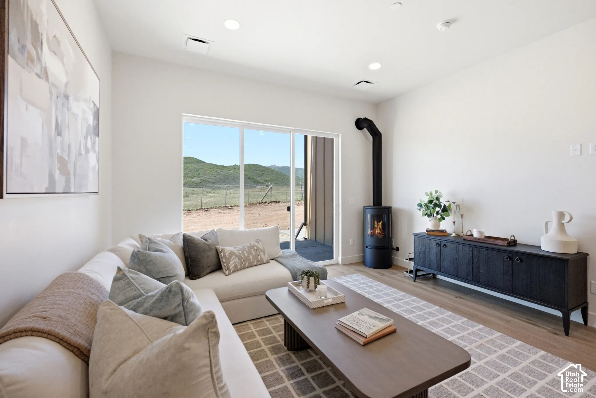 Living area featuring wood-finish flooring, a matte black freestanding cylindrical fireplace, and large glass sliding doors revealing a mountainous landscape