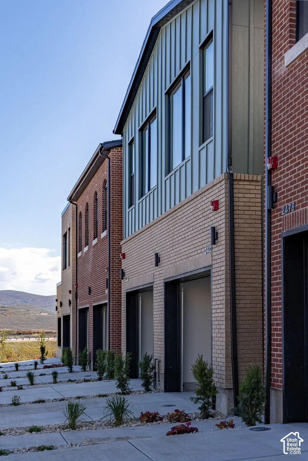Multi-story exterior featuring a mix of red and cream brick masonry, vertical metal panel siding, and integrated garage bays with concrete driveways