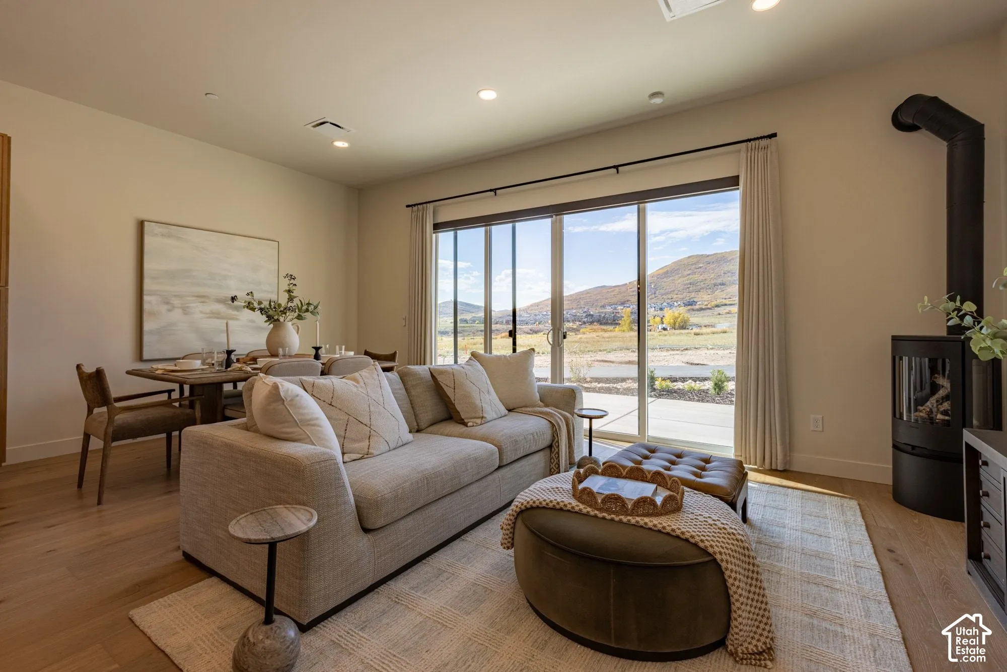 Open-concept living space featuring wood-finish flooring, recessed lighting, a modern black cylindrical freestanding wood-burning stove, and a sliding glass door leading to the exterior with a mountain backdrop
