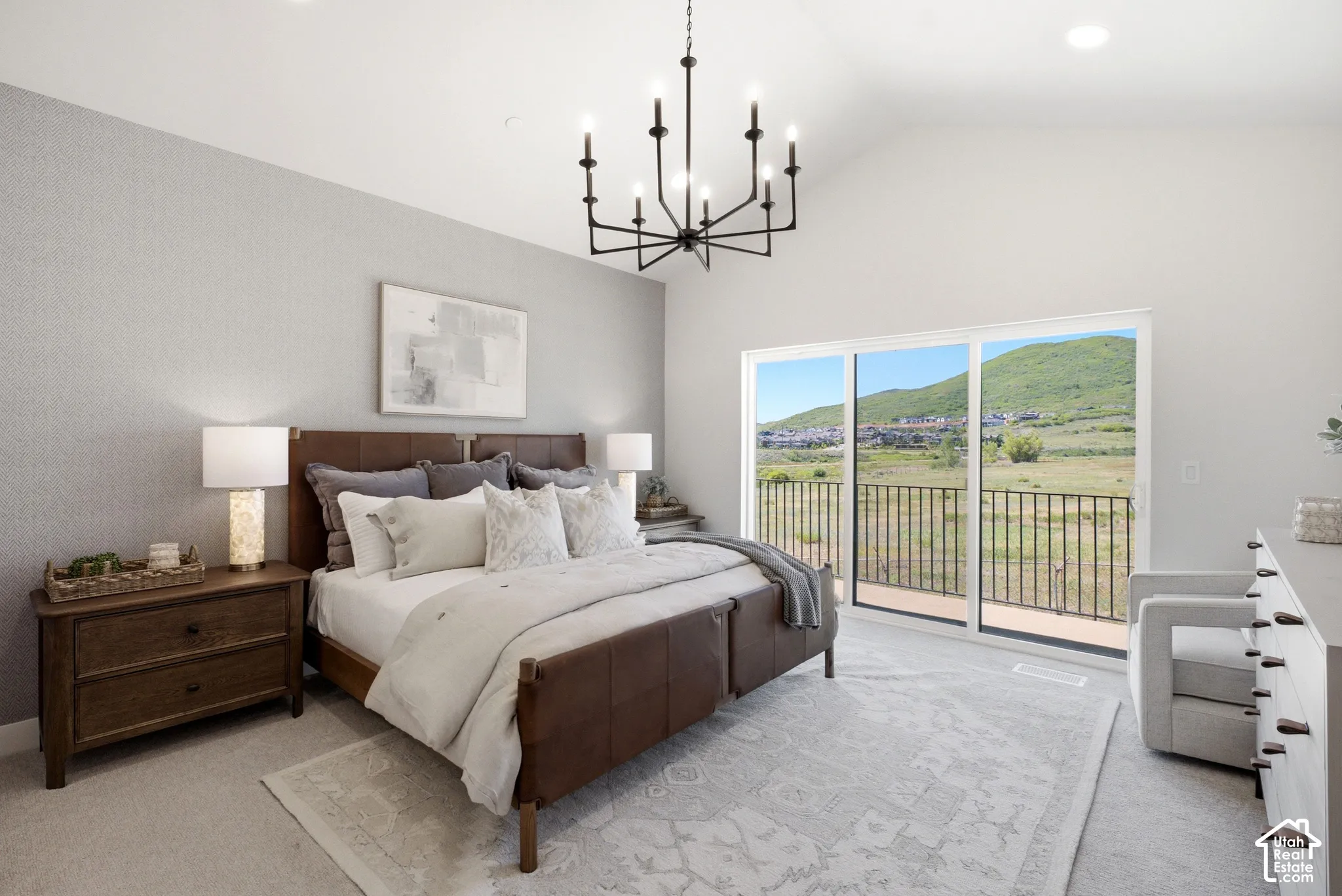 Vaulted ceiling, multi-light chandelier, sliding glass doors, metal balcony railing, and mountain backdrop