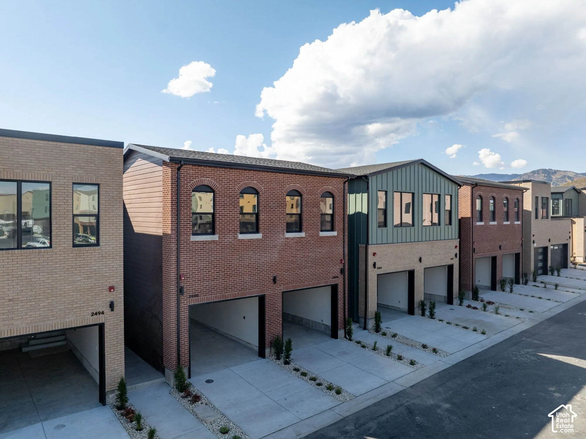 Multi-story exterior featuring red brick and vertical siding, arched window detailing, integrated multi-car garages, and concrete driveways