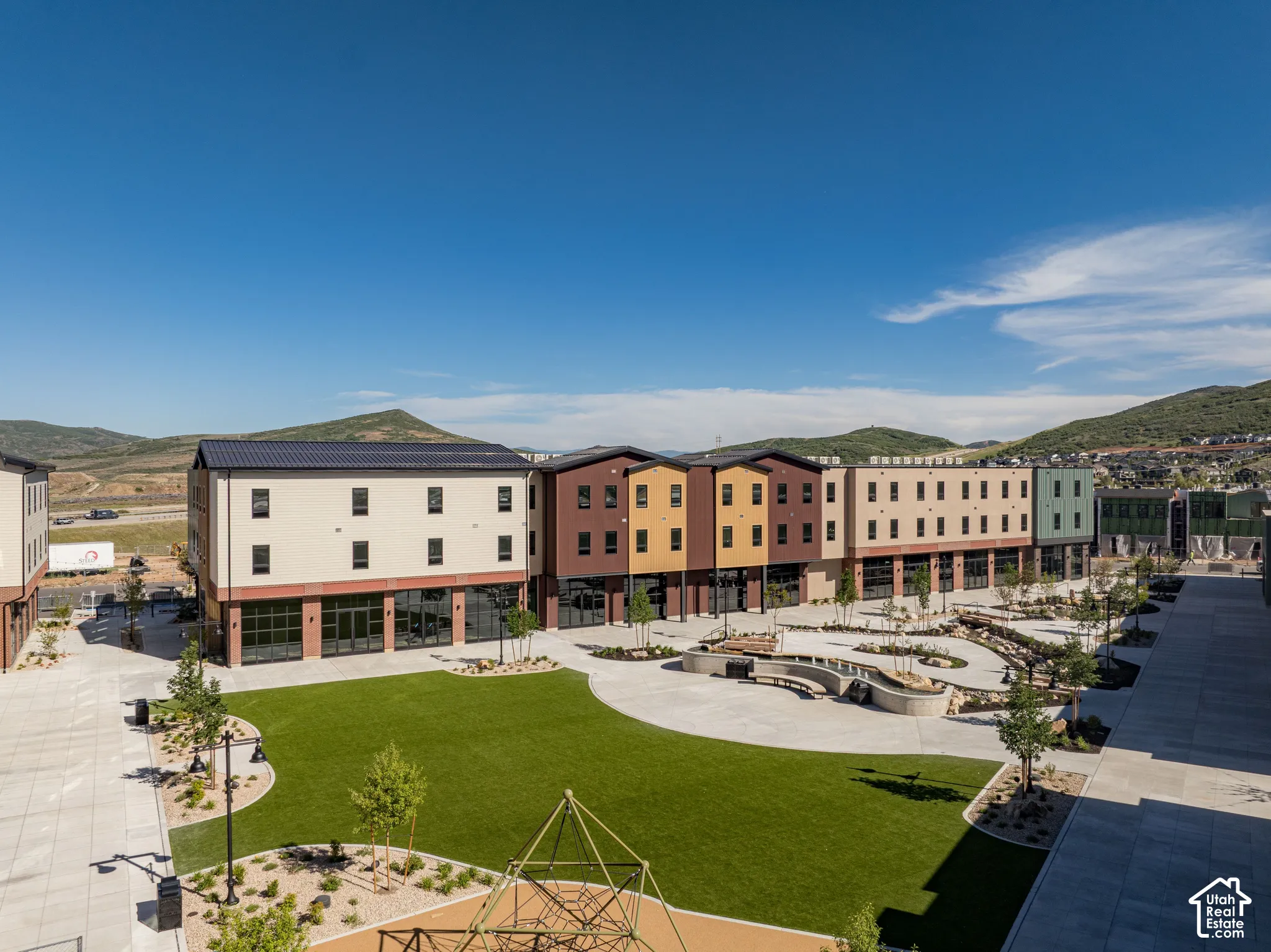 Exterior courtyard featuring a manicured lawn, concrete hardscaping, curved stone retaining wall seating, and mountain backdrop