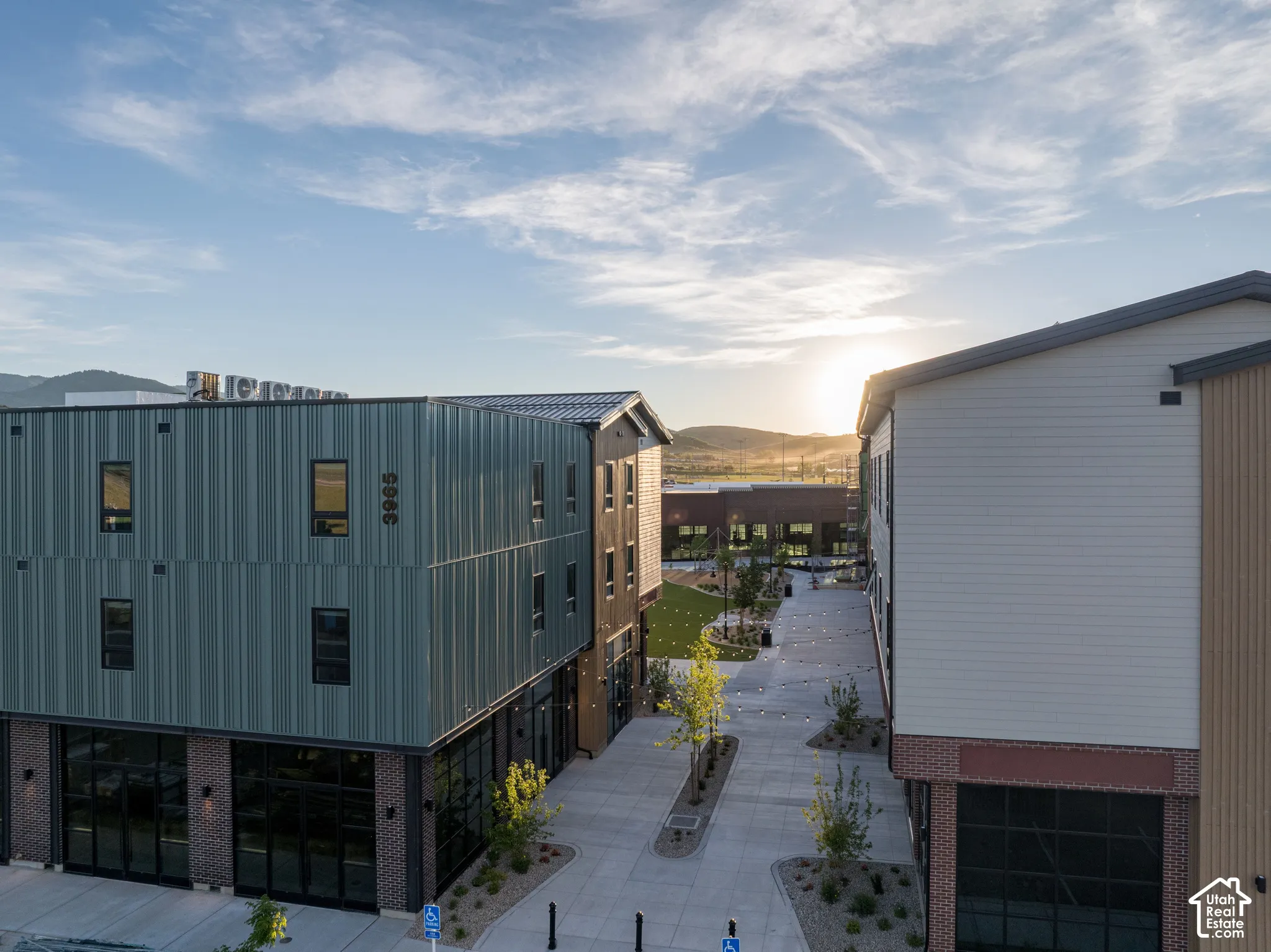Multi-story exterior featuring metal vertical siding, brick masonry, concrete pedestrian pathways, and a landscaped courtyard area