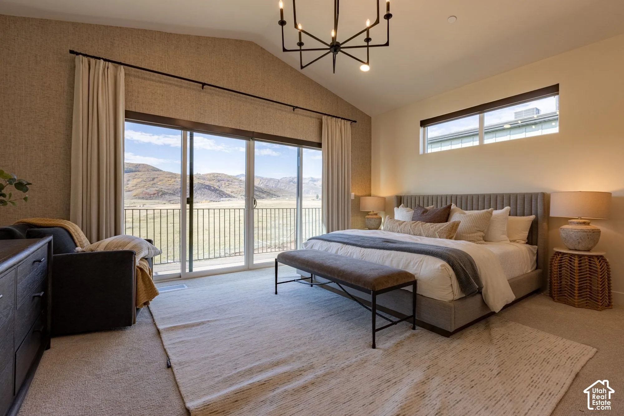 Vaulted ceiling with a multi-arm chandelier, floor-to-ceiling sliding glass doors, transom window, and exterior metal railing with mountain scenery