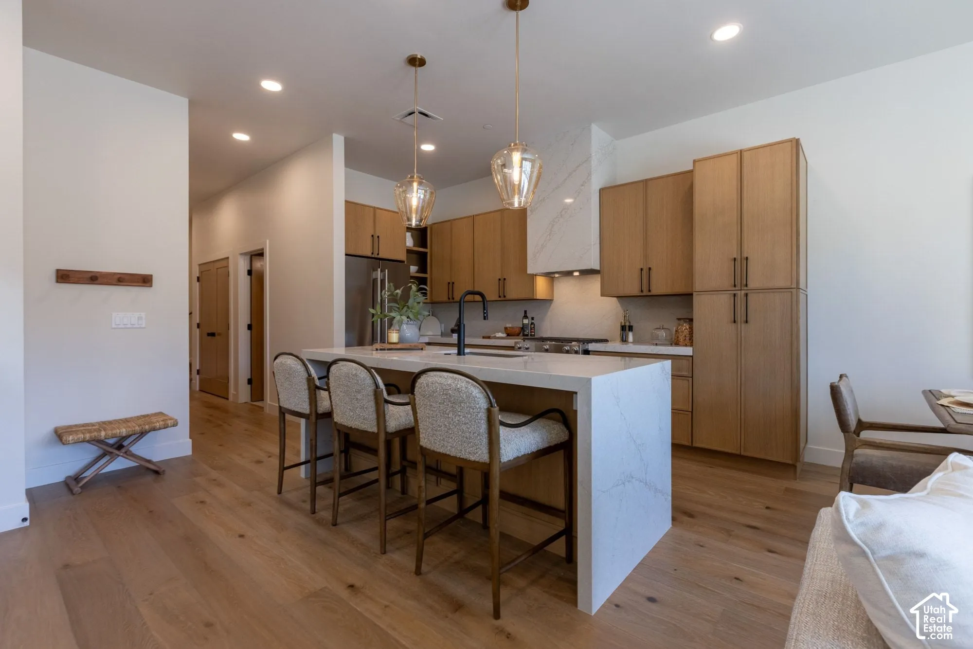 Kitchen featuring flat-panel wood cabinetry, a waterfall-edge island with a quartz countertop, integrated hood vent, wood-finish flooring, and pendant lighting