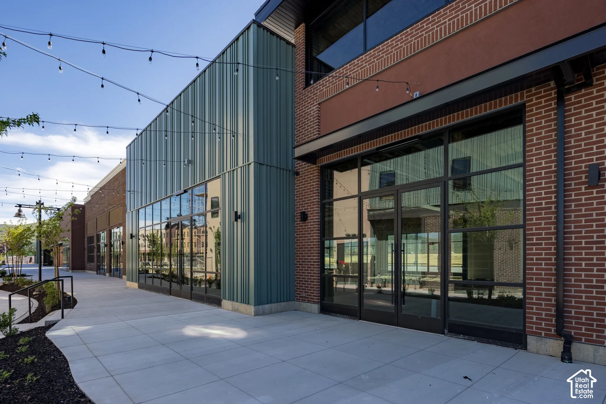 Commercial storefront featuring a brick and vertical metal paneled exterior, expansive floor-to-ceiling glass windows, double glass entrance doors, and a concrete walkway