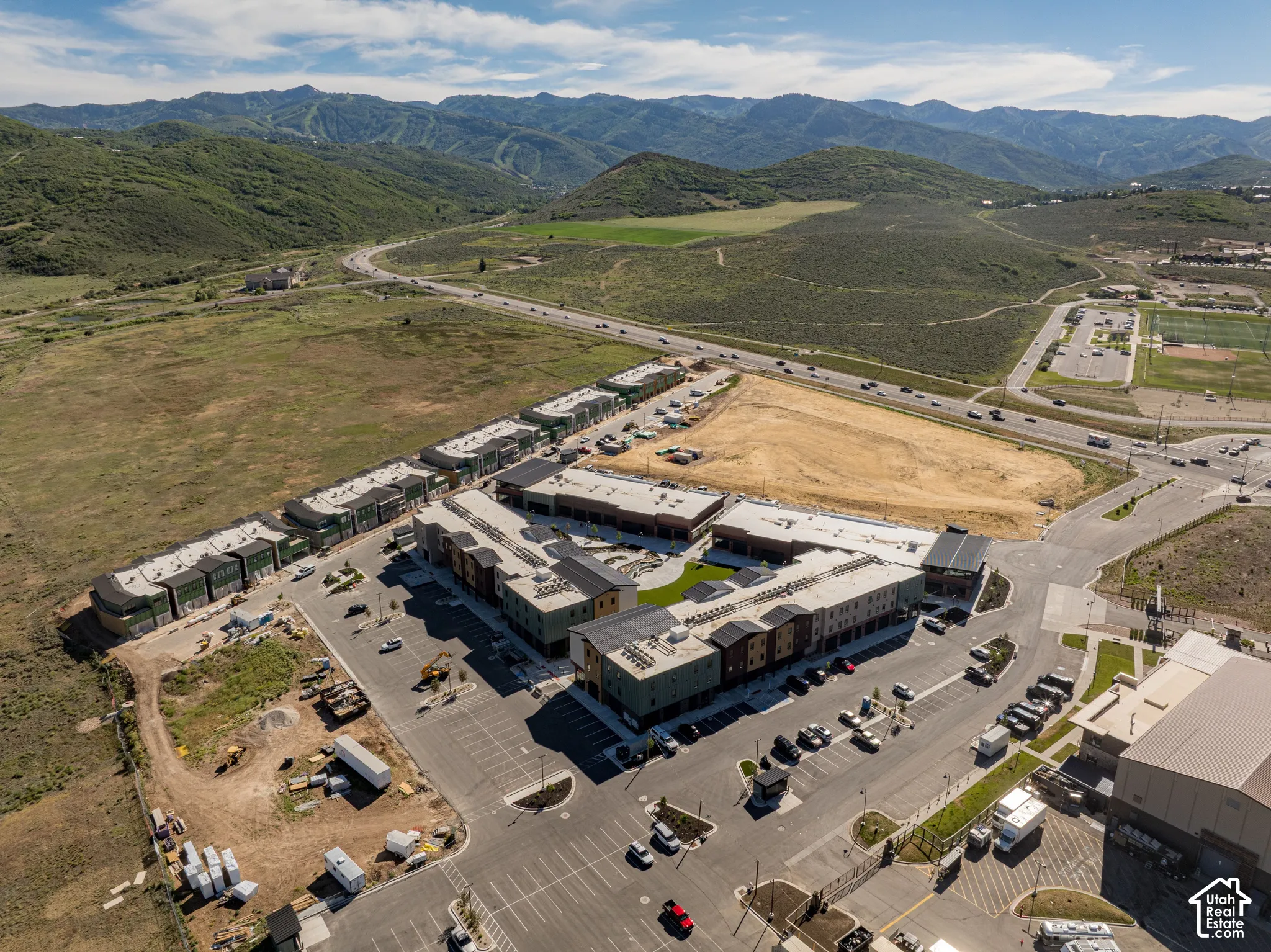 Aerial perspective of a multi-building complex featuring flat-roof architecture, mixed-material facades, designated surface parking, and mountainous terrain