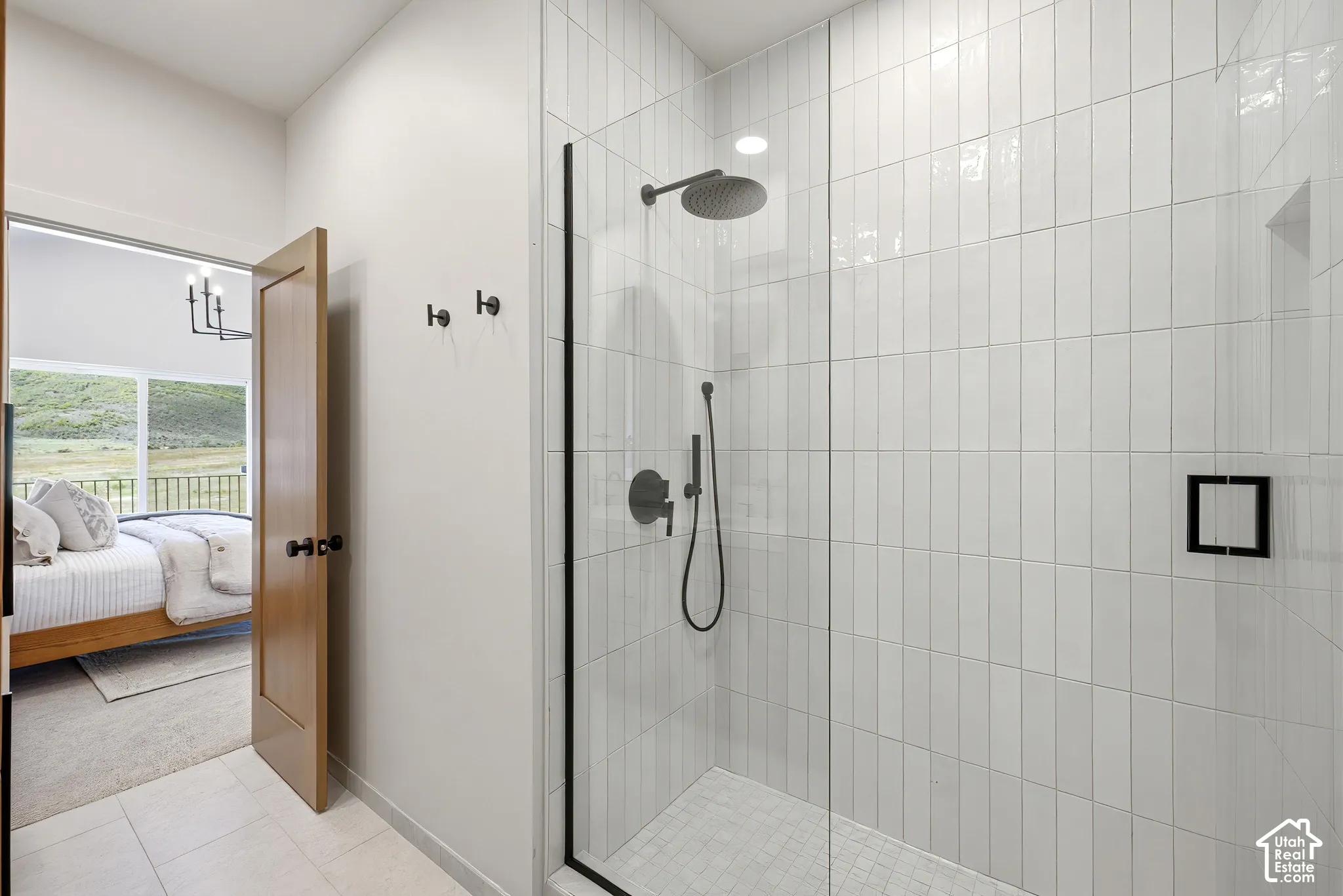 Walk-in shower featuring vertical white wall tile, a frameless glass enclosure, matte black rainfall shower head, handheld sprayer, and an integrated recessed niche