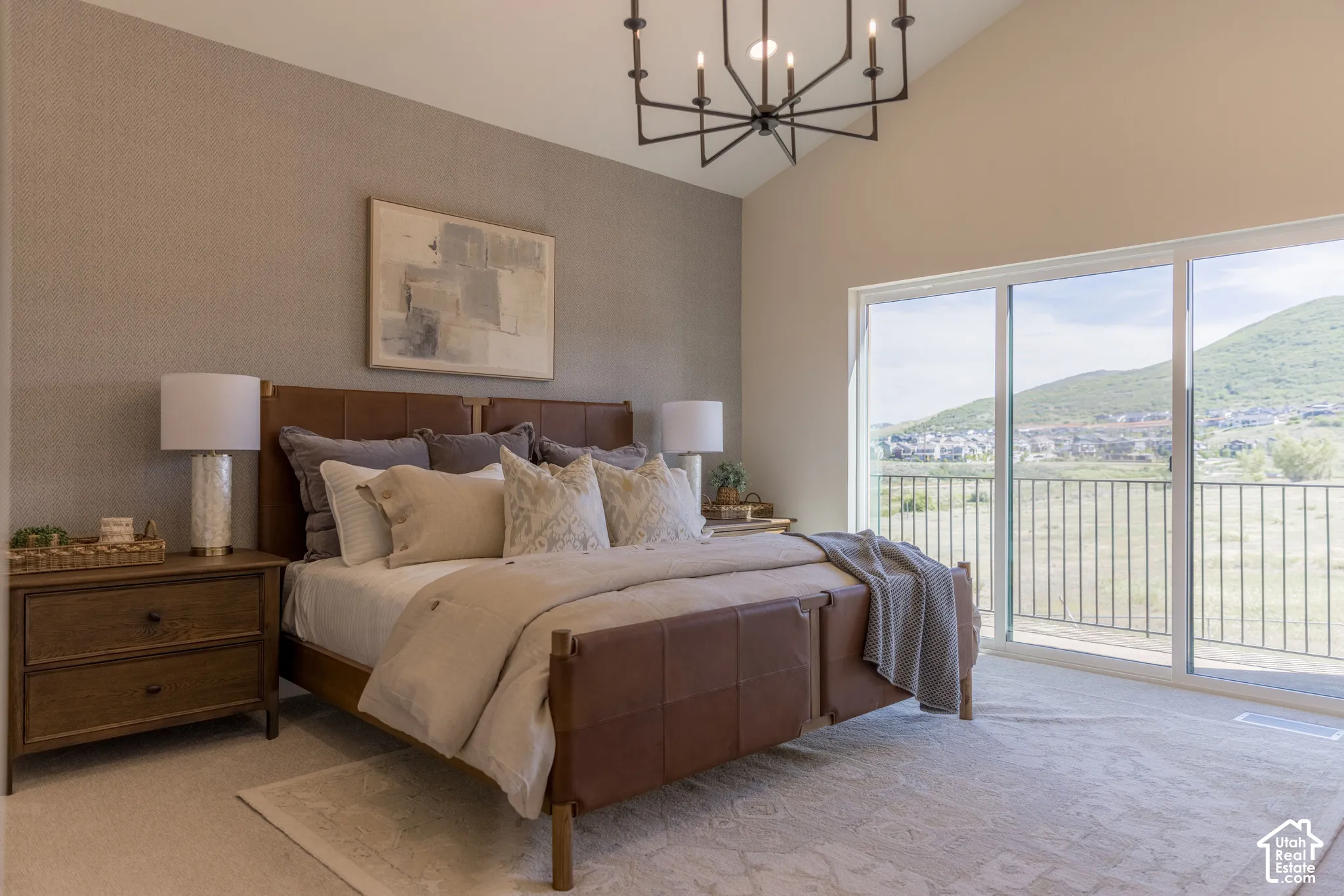 Vaulted ceilings featuring a black metal chandelier, accented by a textured feature wall and large sliding glass doors opening to a metal-railed balcony with mountain scenery